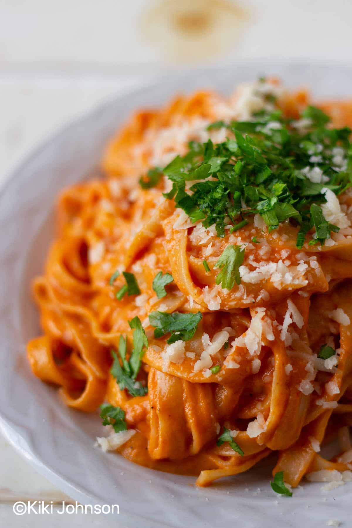 roasted red bell pepper pasta on a white plate topped with chopped basil 