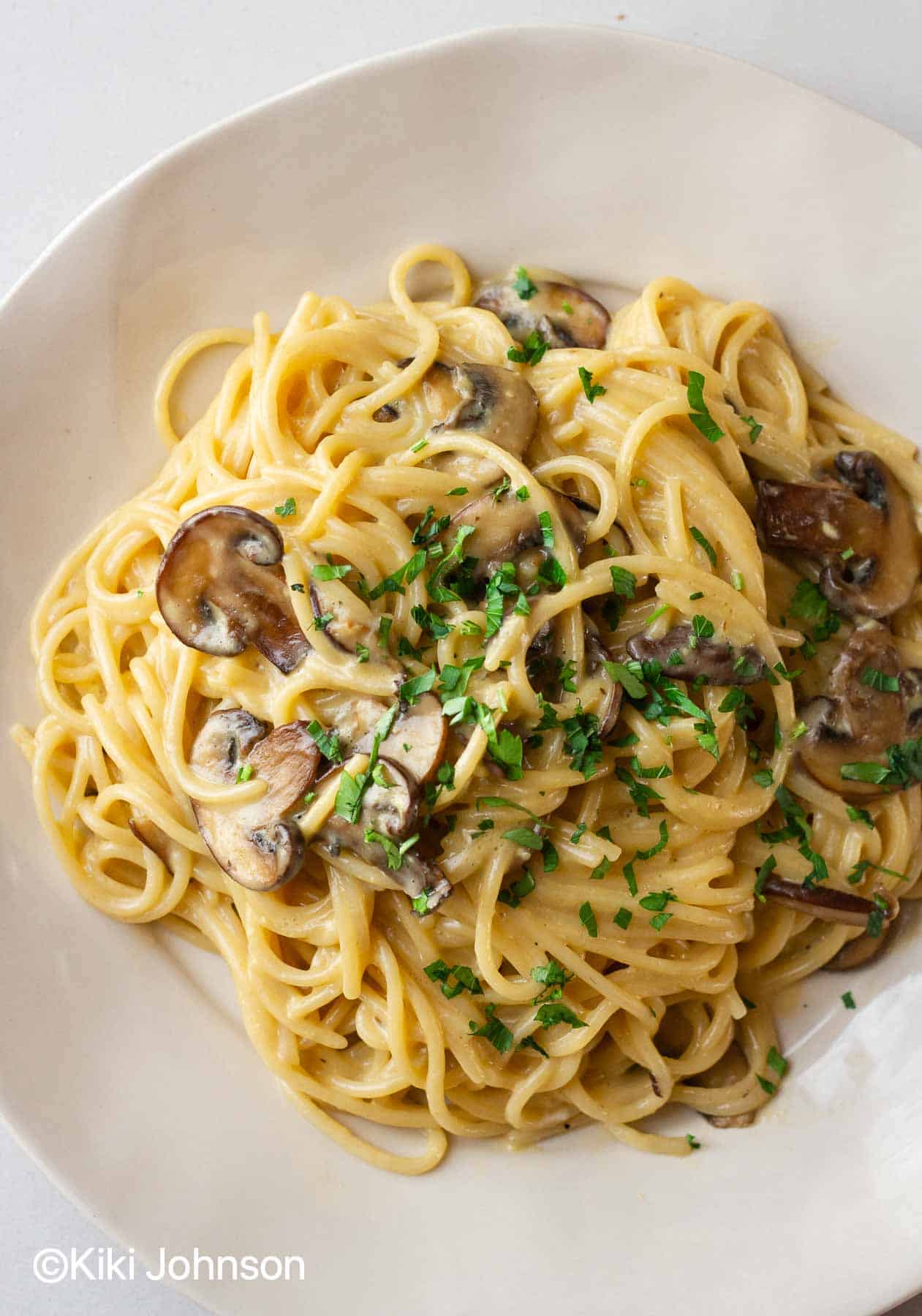 a plate with mushroom pasta carbonara sprinkled with parsley 