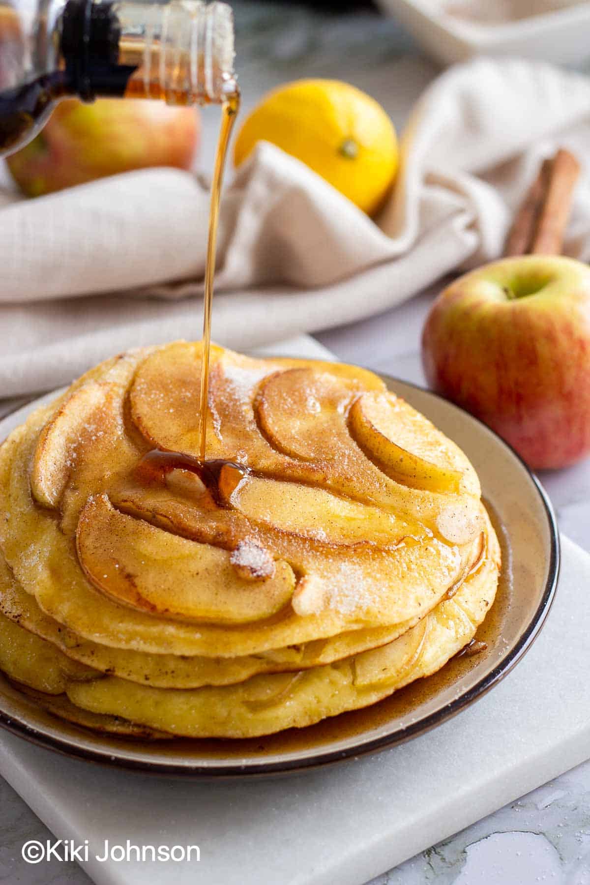 maple syrup being drizzled over a stack of Grannys German Apple Pancakes