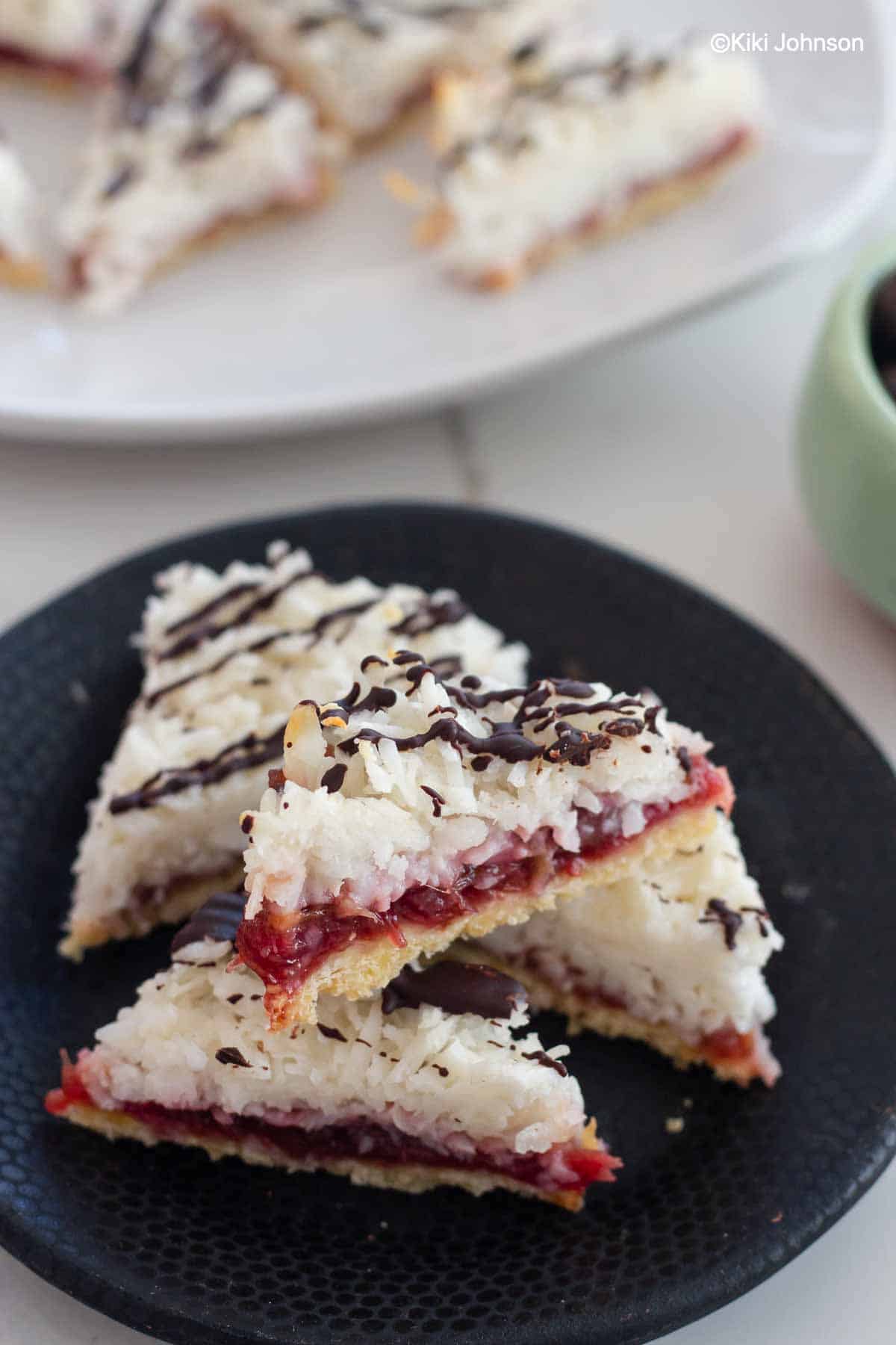 German Cookies with jam and a layer of coconut macaroons on a black plate