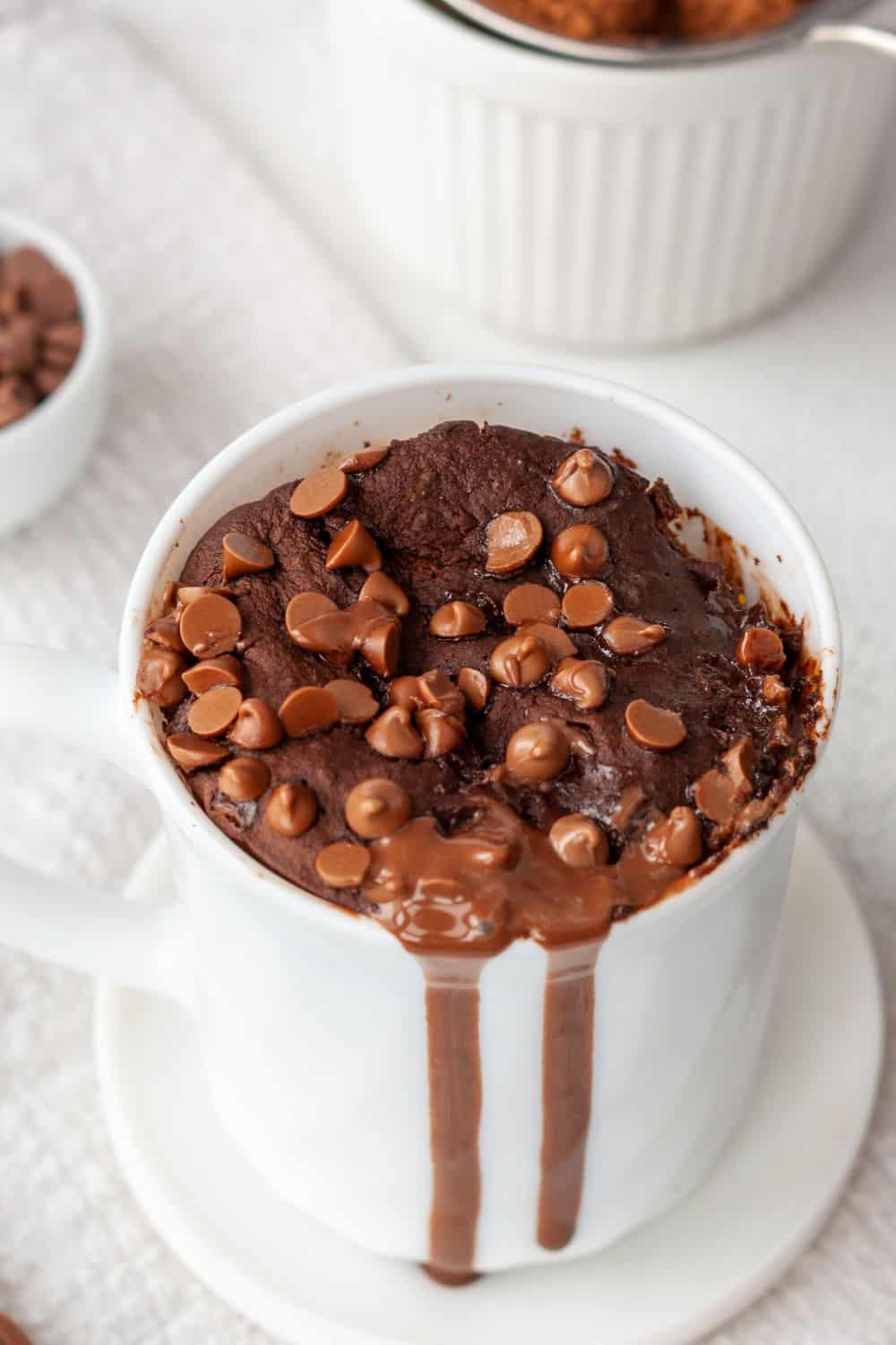 a vegan brownie in a mug with chocolate sauce and chocolate chips