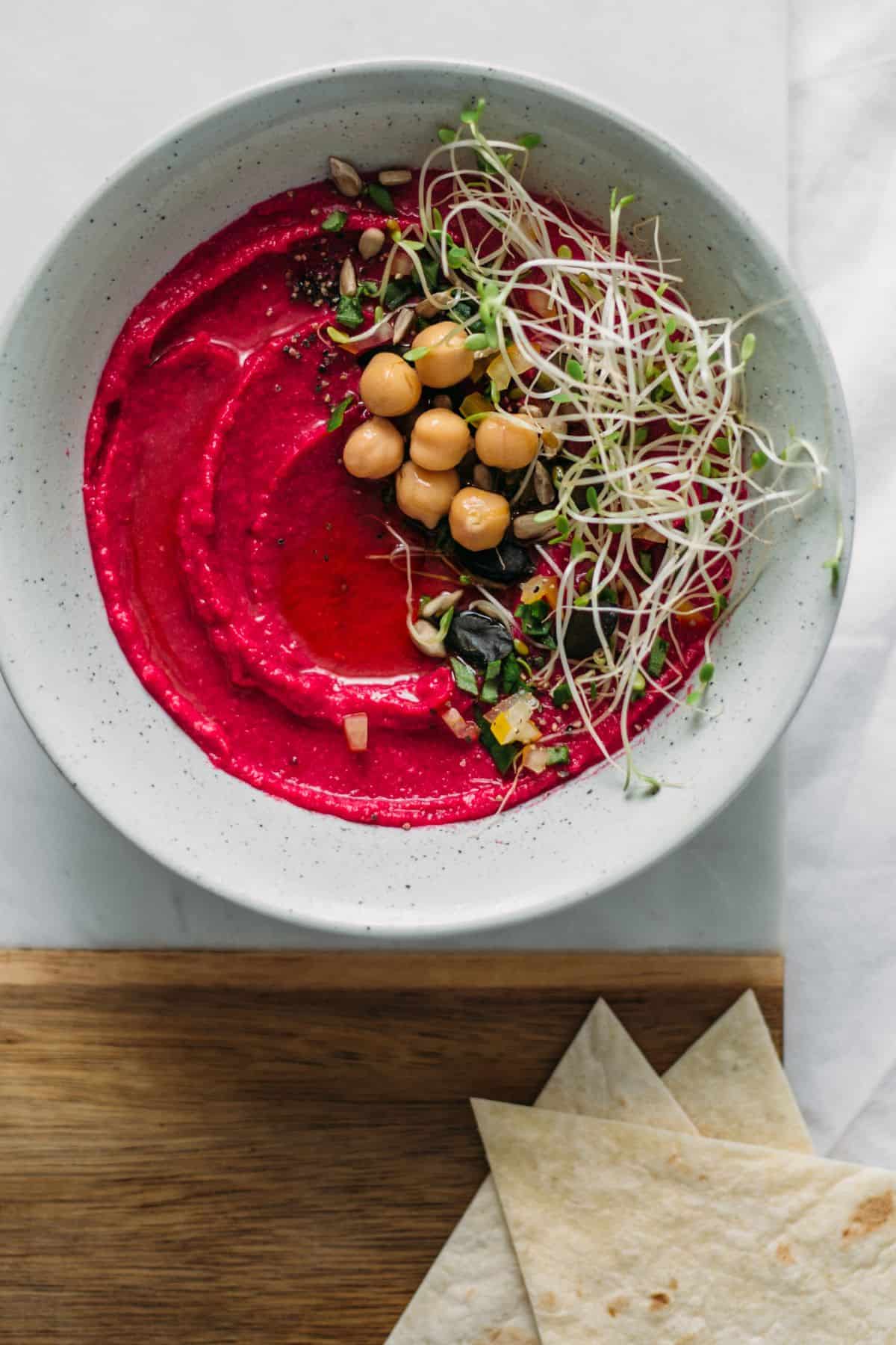 a serving platter with roasted beetroot dip topped with chickpeas and sprouts
