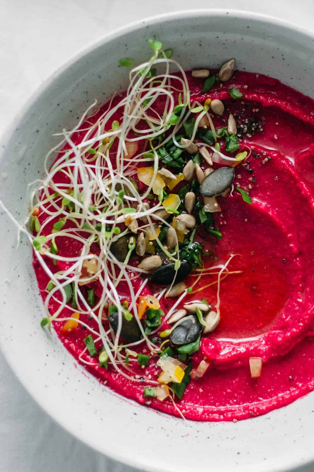 roasted beetroot hummus by ottolenghi in a pale grey serving platter topped with seeds and sprouts