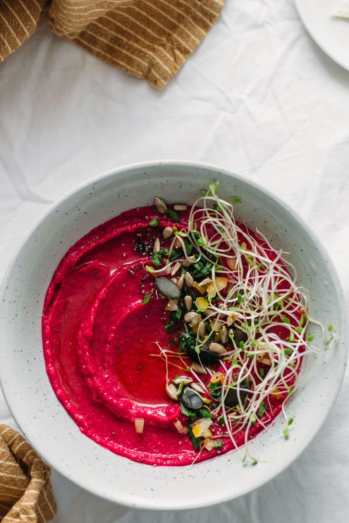 a platter with roasted beetroot hummus topped with sprouts and nuts 