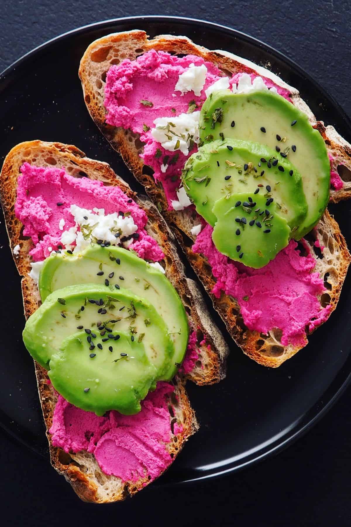 zwei Scheiben Brot mit rote Beete Hummus bestrichen und mit Avocadoscheiben belegt