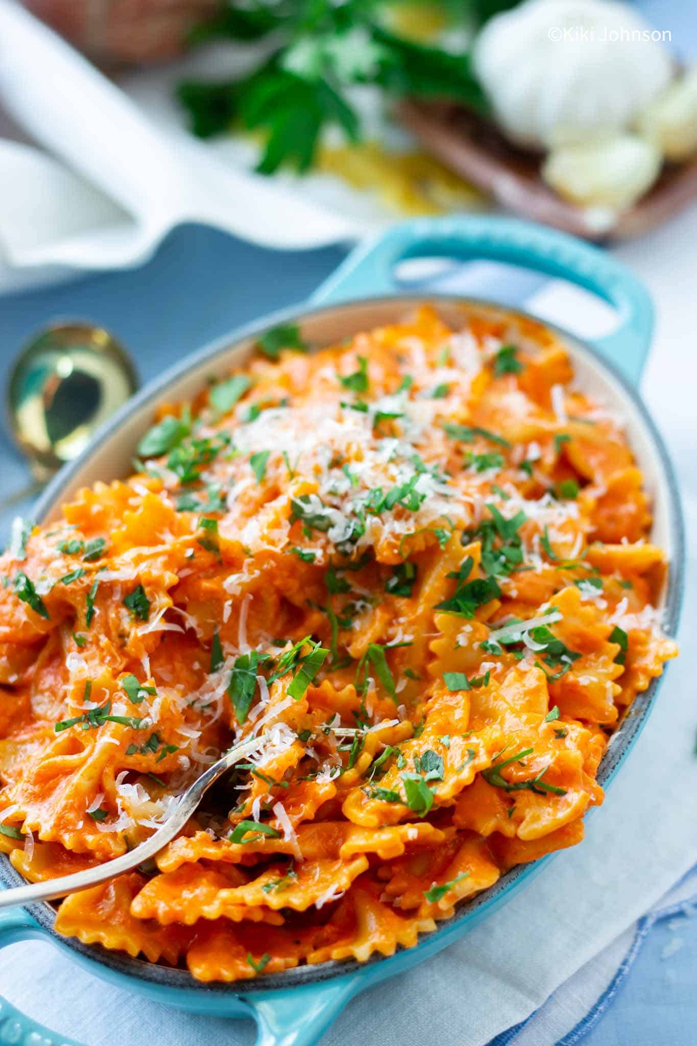 Farfalle Nudeln mit Tomaten Sahne Soße in einer kleinen blauen Auflaufform mit Basilikum und Parmesan bestreut