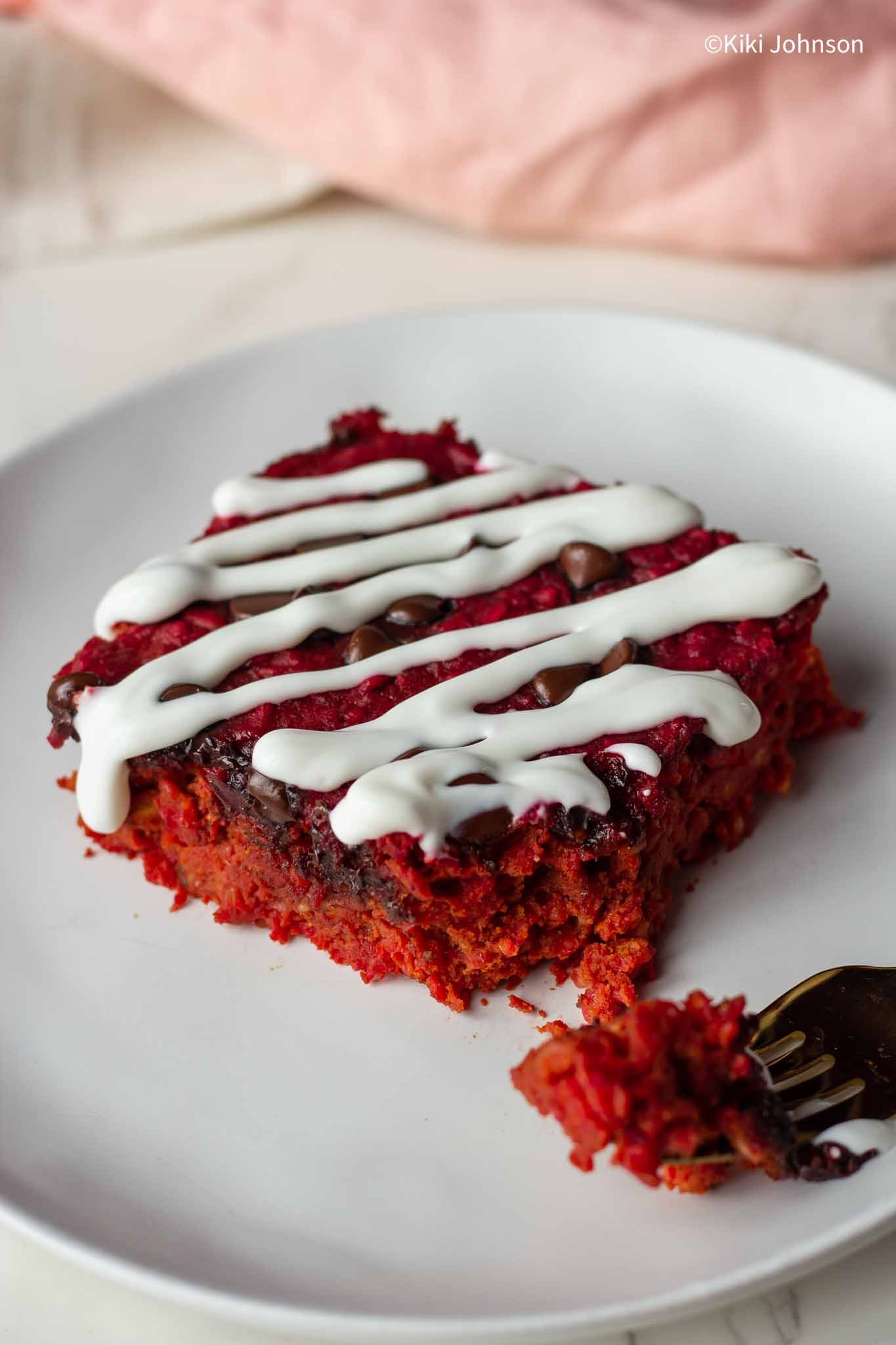 a square of high protein beet oatmeal bake on a white plate drizzled with Greek yogurt 