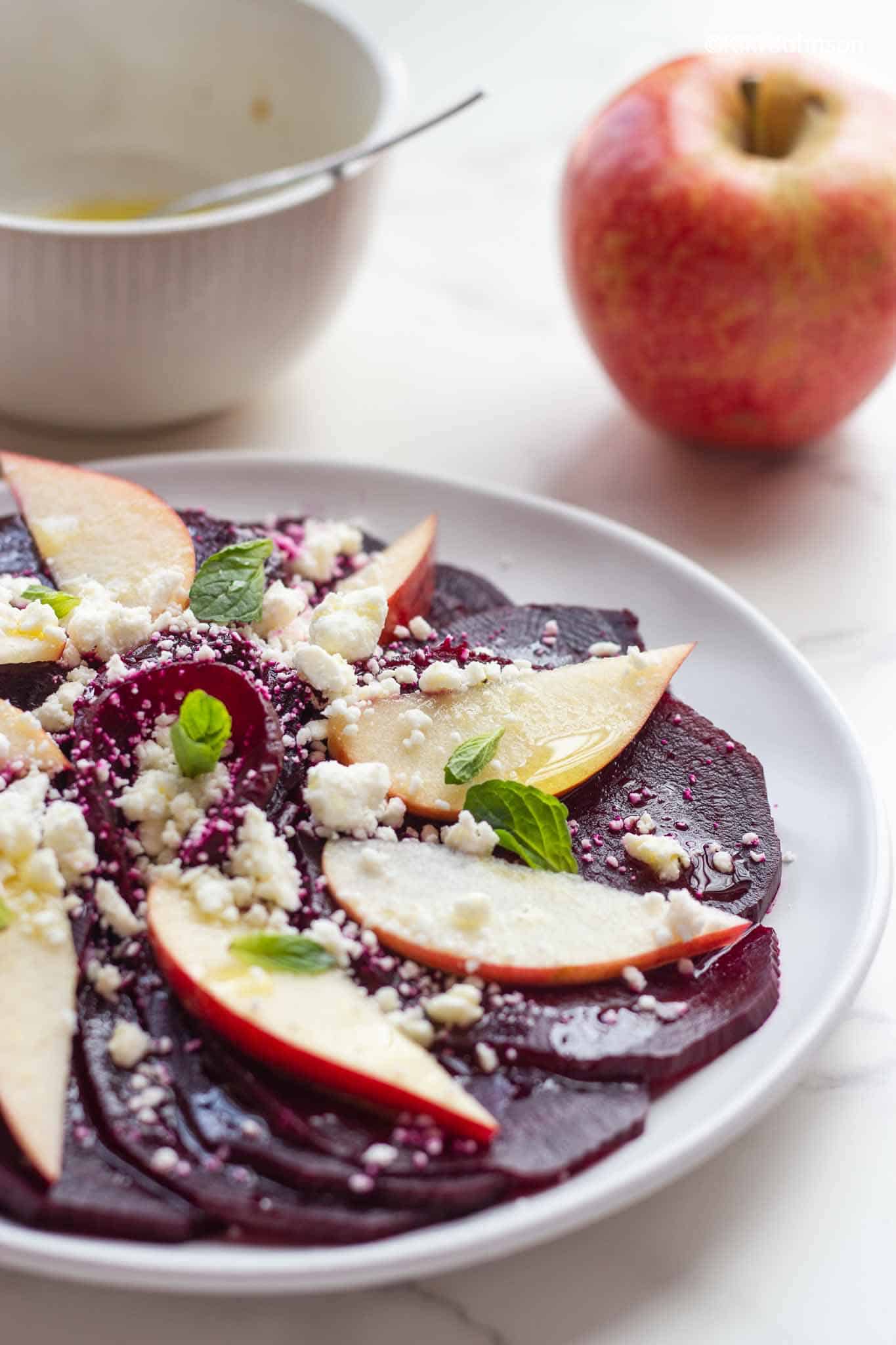 side view of a beet and apple salad topped with feta cheese and mint leaves 