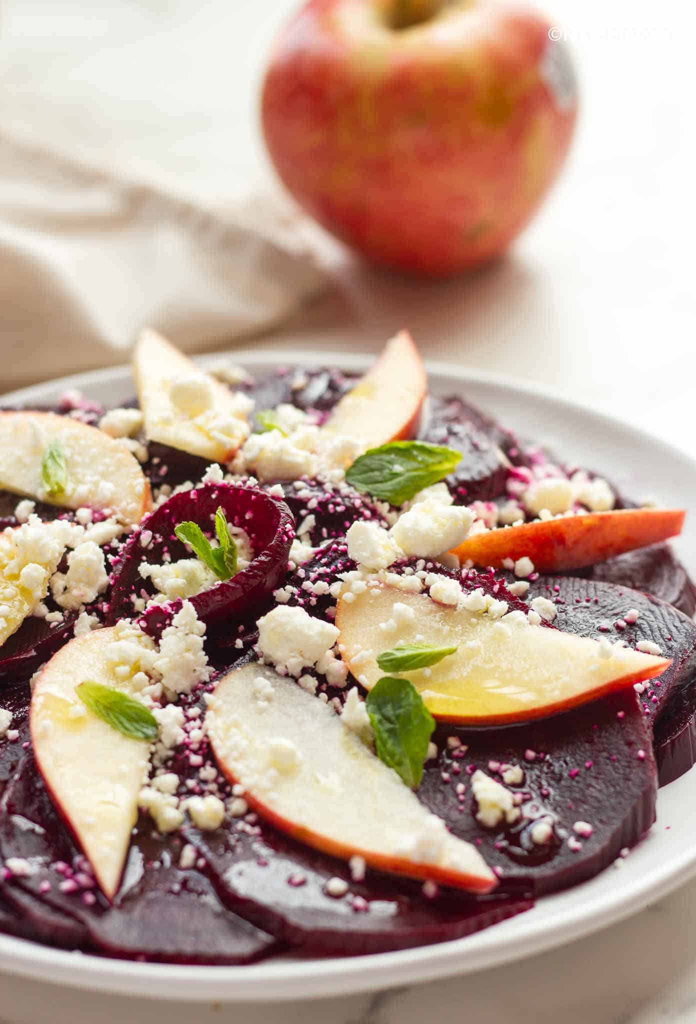 side view of beet and apple salad topped with crumbled feta and mint leaves 