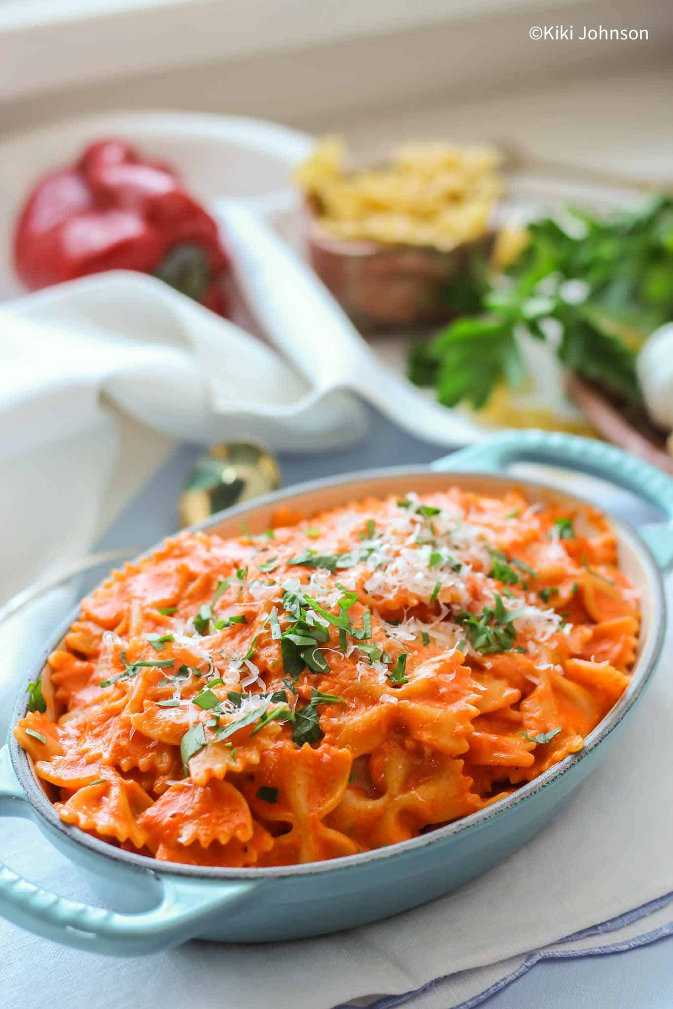 a platter with creamy tomato basil pasta topped with grated parmesan cheese and basil 