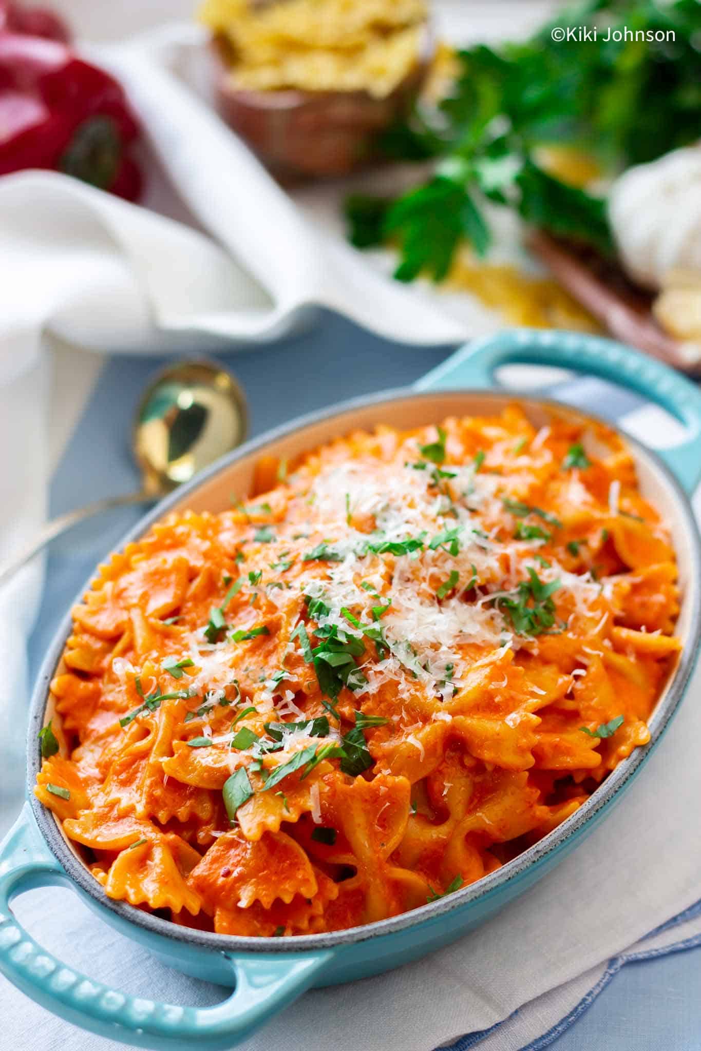 creamy tomato basil pasta served in a a blue casserole dish sprinkled with parmesan cheese and basil 