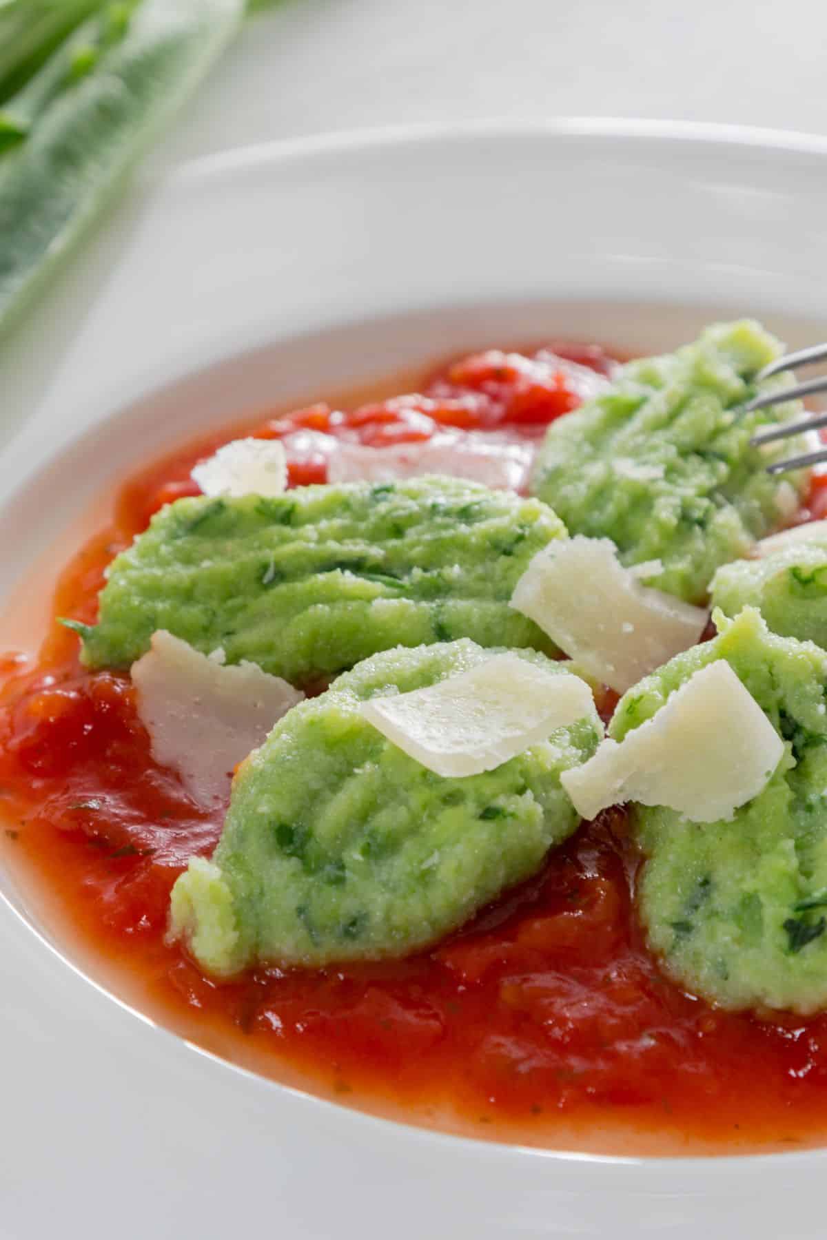 a fork piercing into homemade wild garlic gnocchi served with tomato sauce