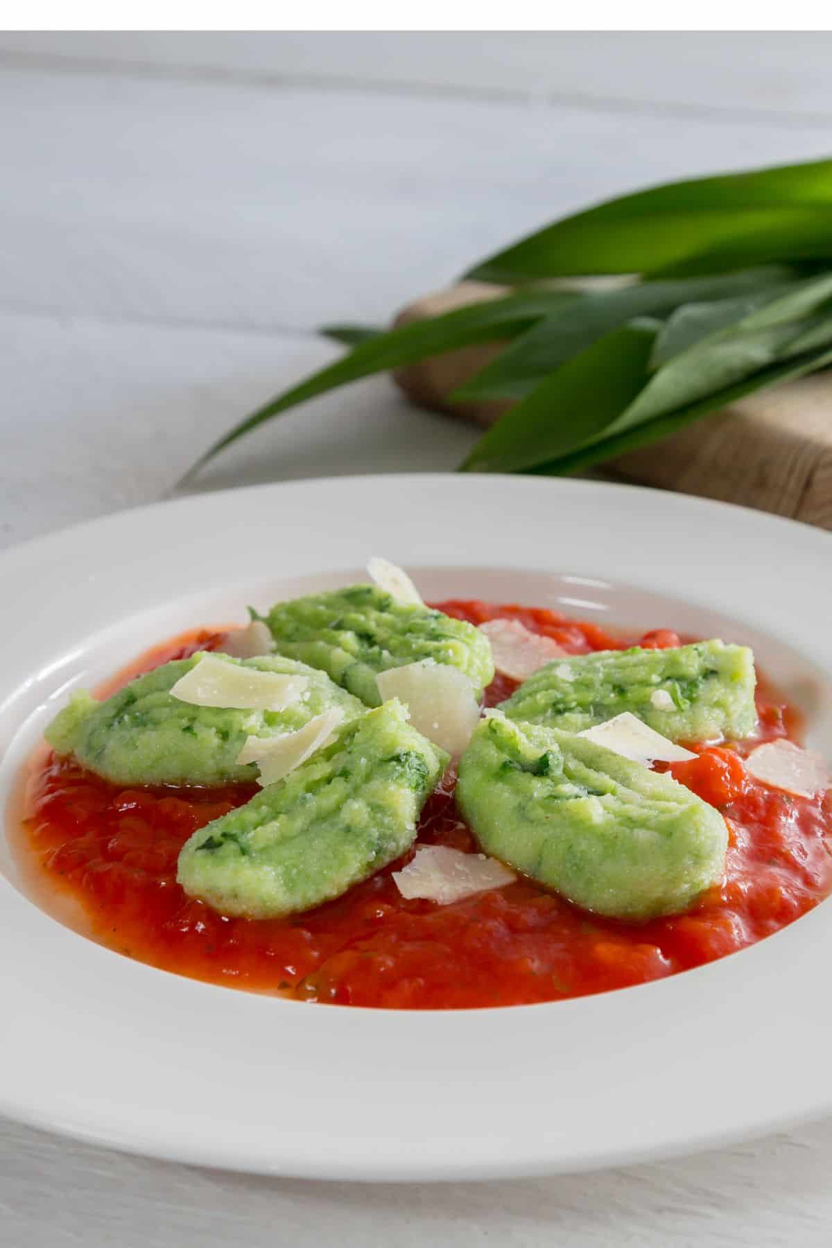 a plate with wild garlic gnocchi served on tomato sauce and topped with parmesan