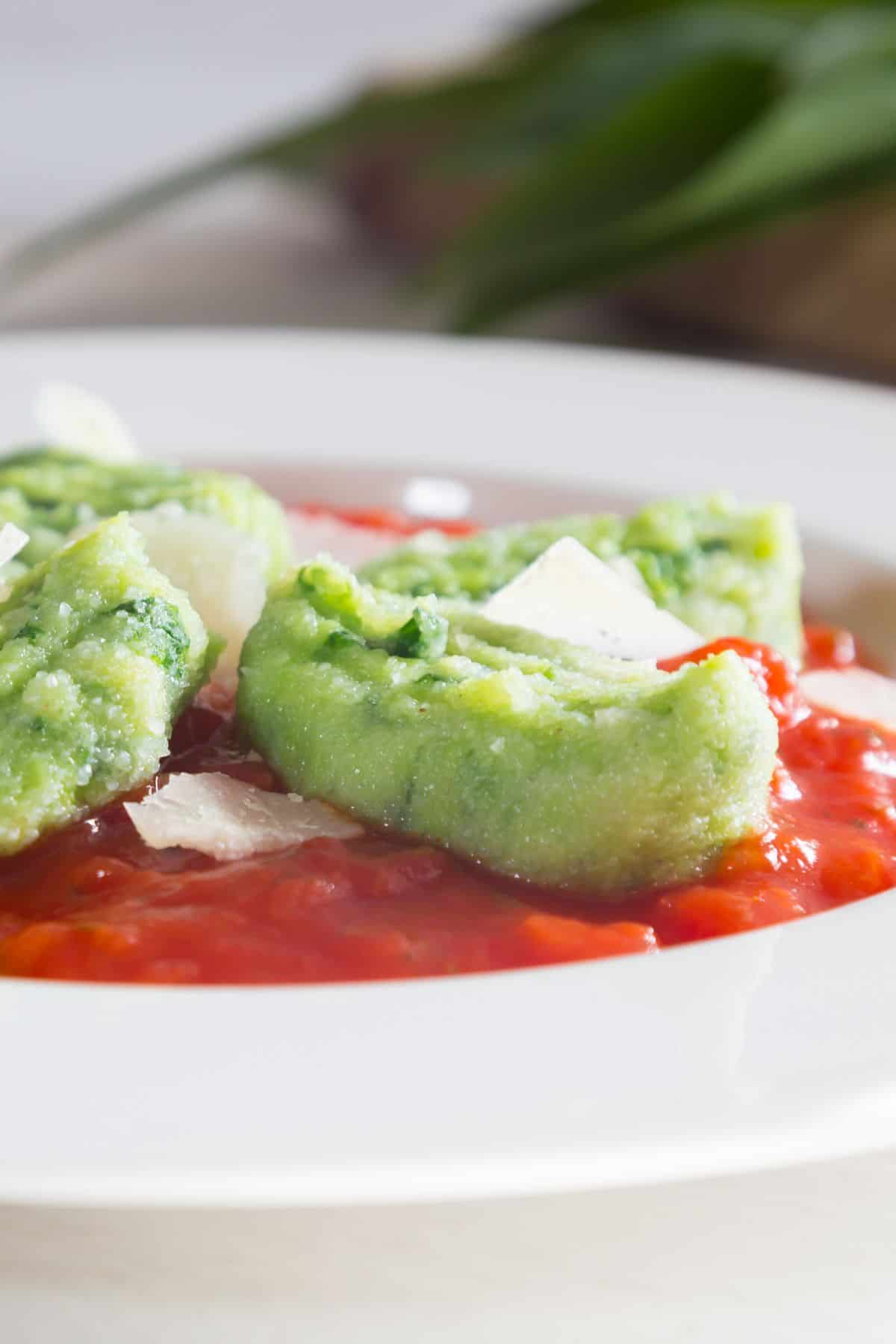 close-up sideview of wild garlic gnocchi over tomato sauce with shaved parmesan