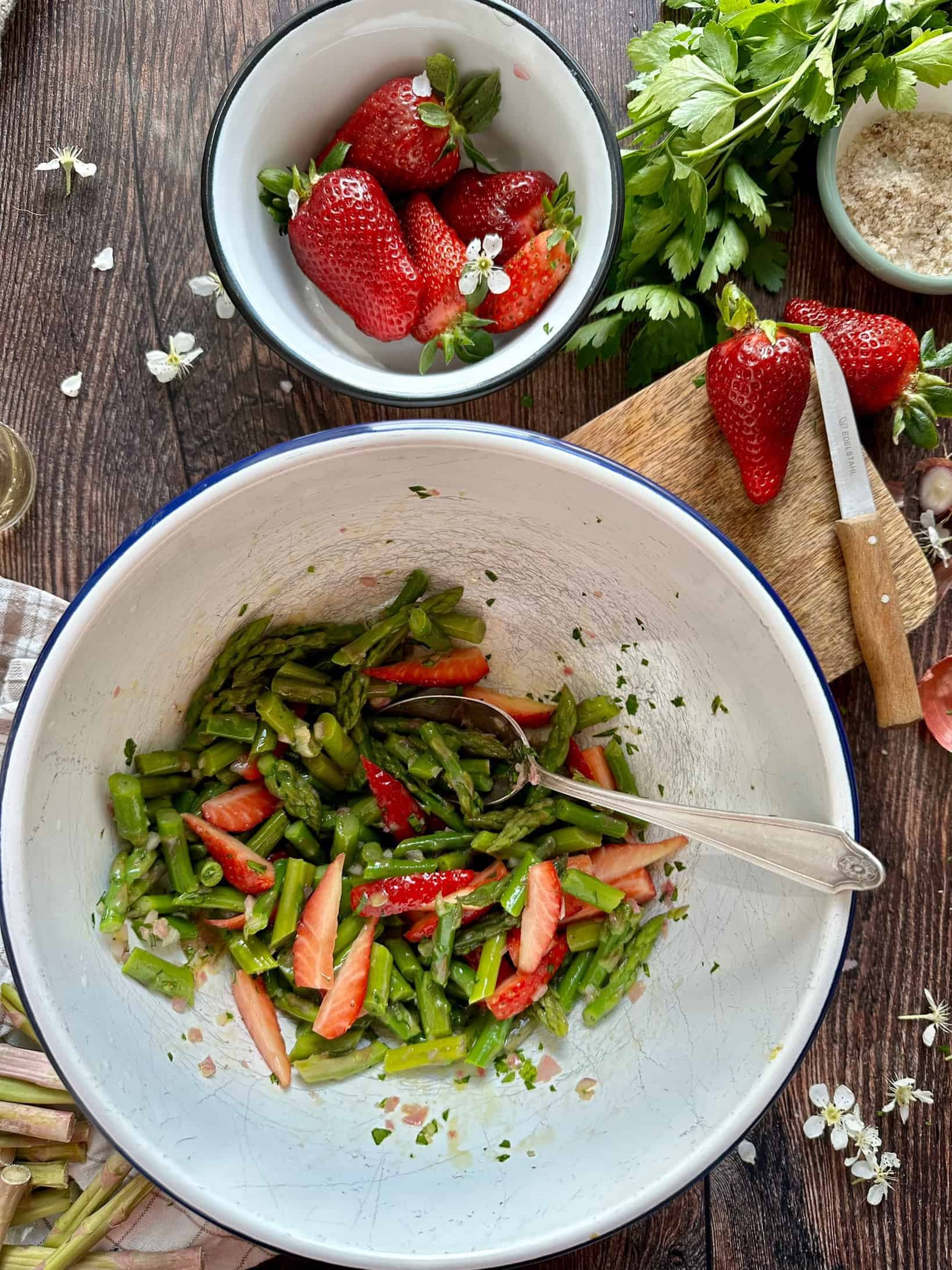 Eine Salatschüssel mit Spargelstücken und Erdbeerscheiben und Salatdressing. 