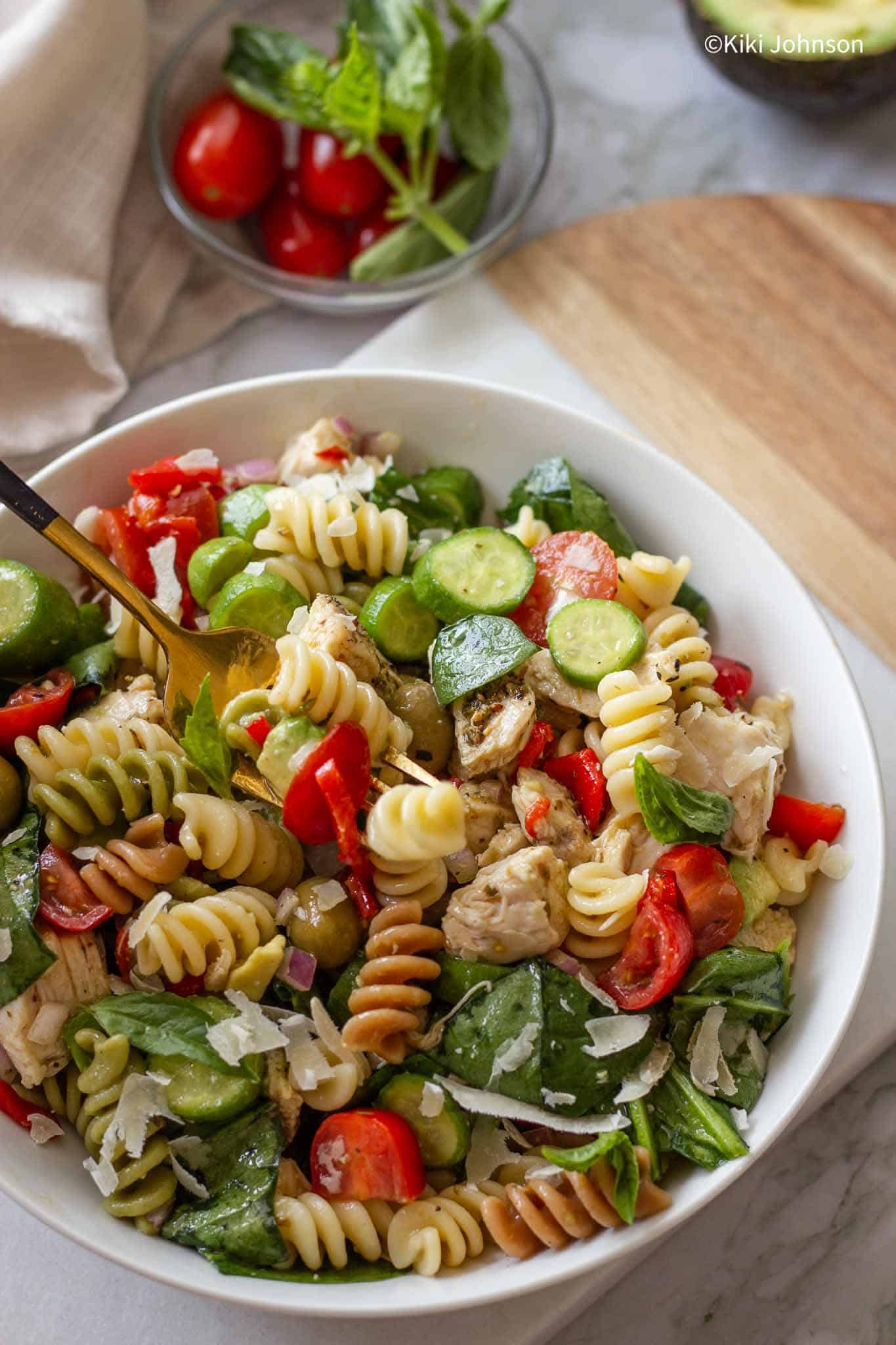 a bowl of chicken pesto pasta salad with cocktail tomatoes and parmesan cheese