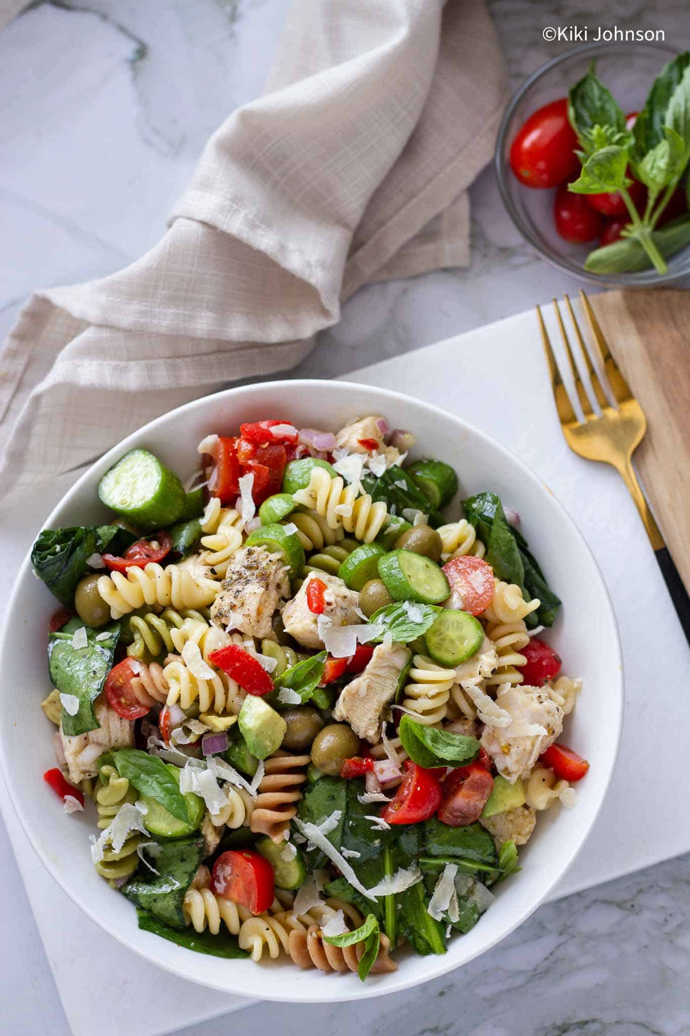 schneller Nudelsalat mit Hähnchen, Tomaten, Gurken und Basilikum in einem weißen Teller 