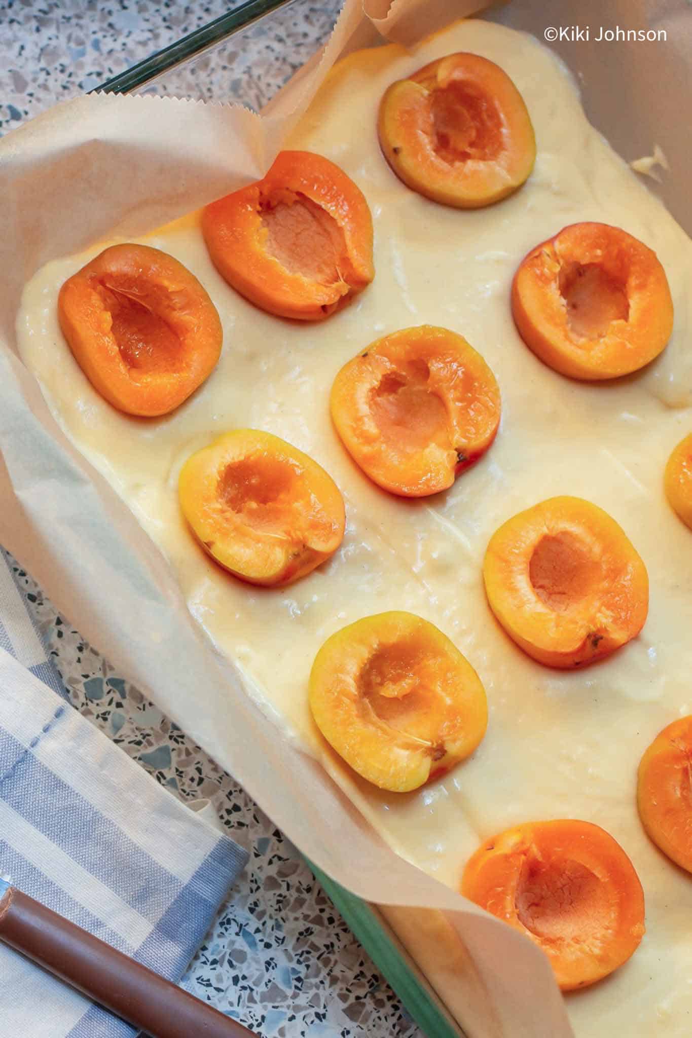 Frische Aprikosenhälften werden auf Rührteig in einem Backblech platziert um Aprikosenkuchen zu backen.