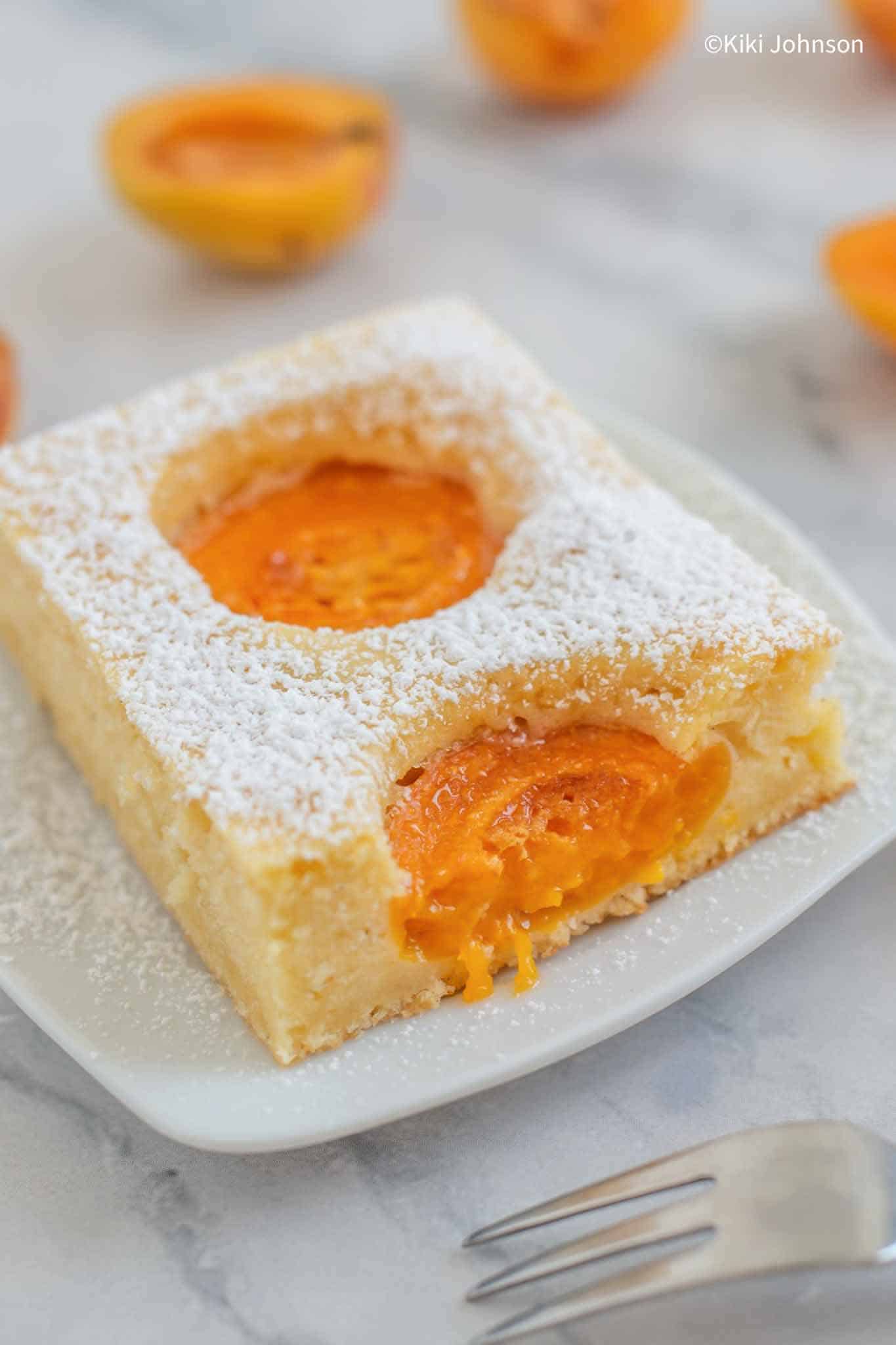 a slice of German Apricot Sponge Cake dusted with icing sugar with a fork on the side.