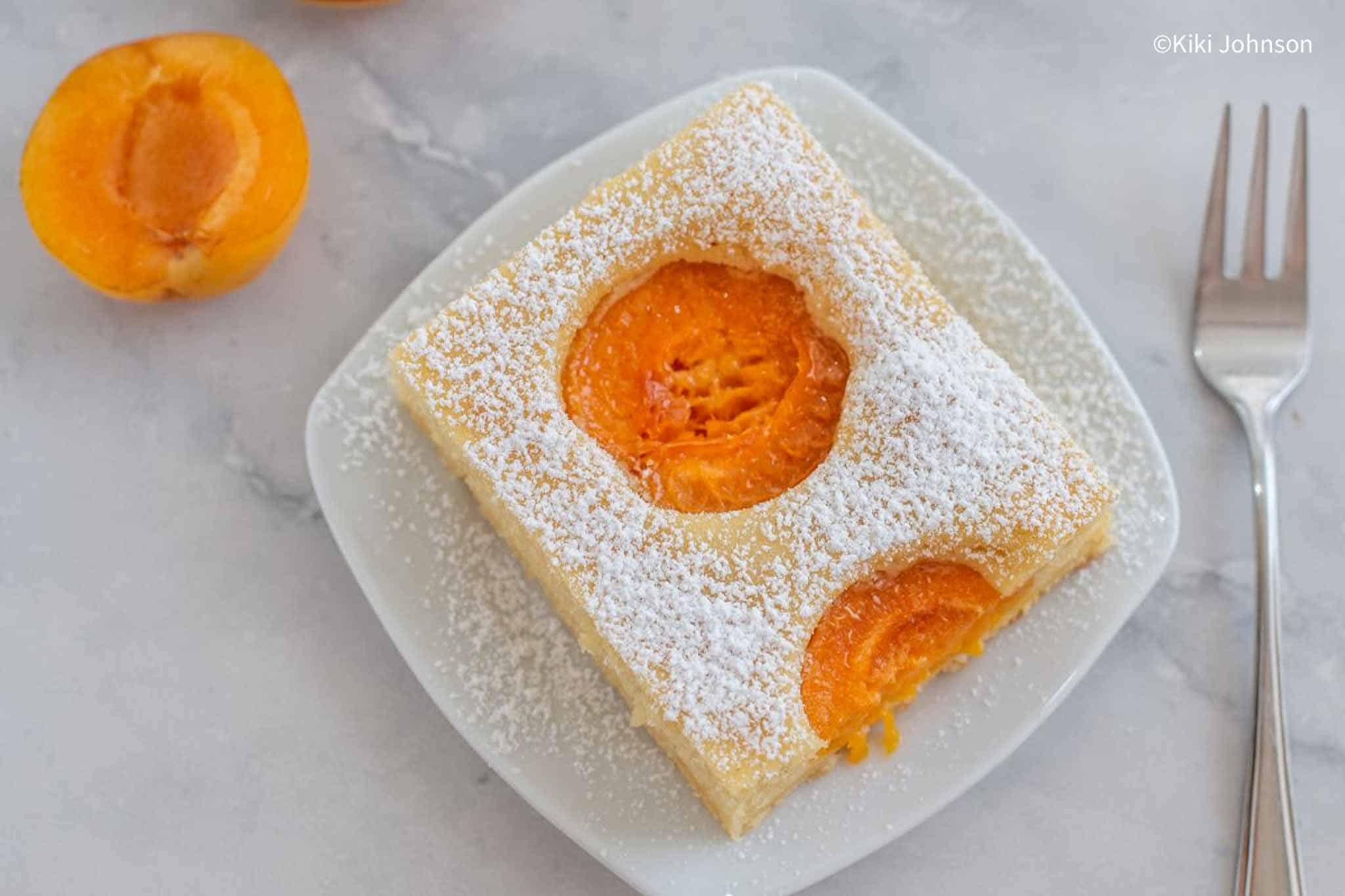 a slice of apricot sponge cake with fresh apricot halves on the side.