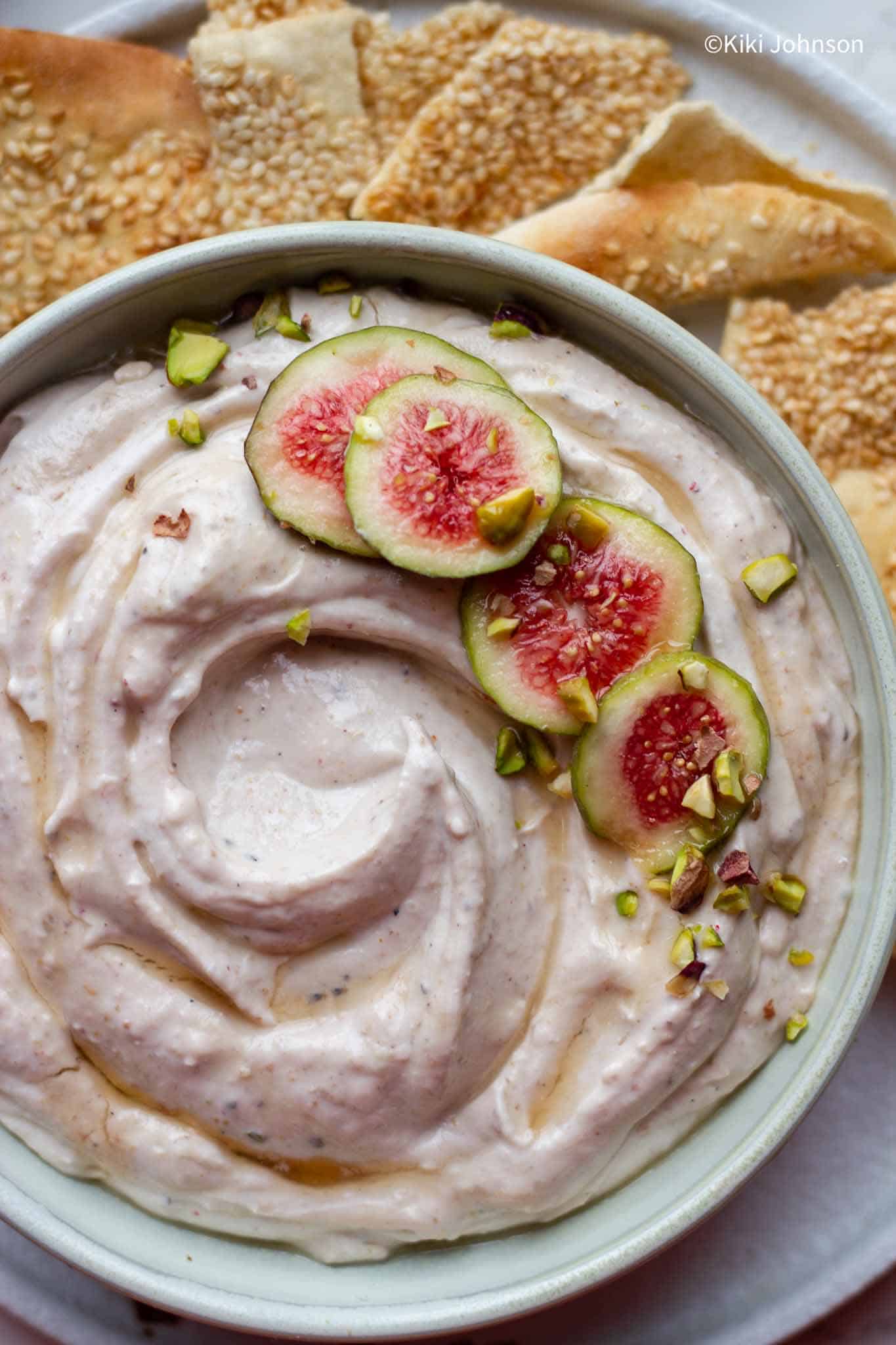 a platter of fresh fig spread made with goat cheese topped with honey, pistachios and fresh figs.