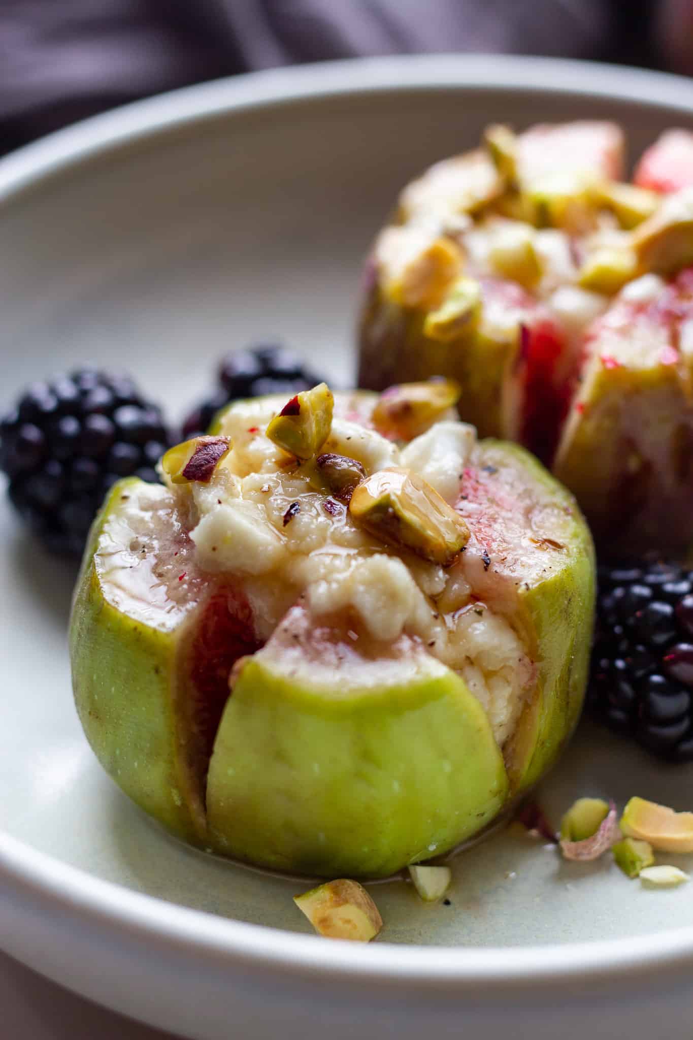 baked figs stuffed with goat cheese, nuts and drizzled with honey on a small plate.