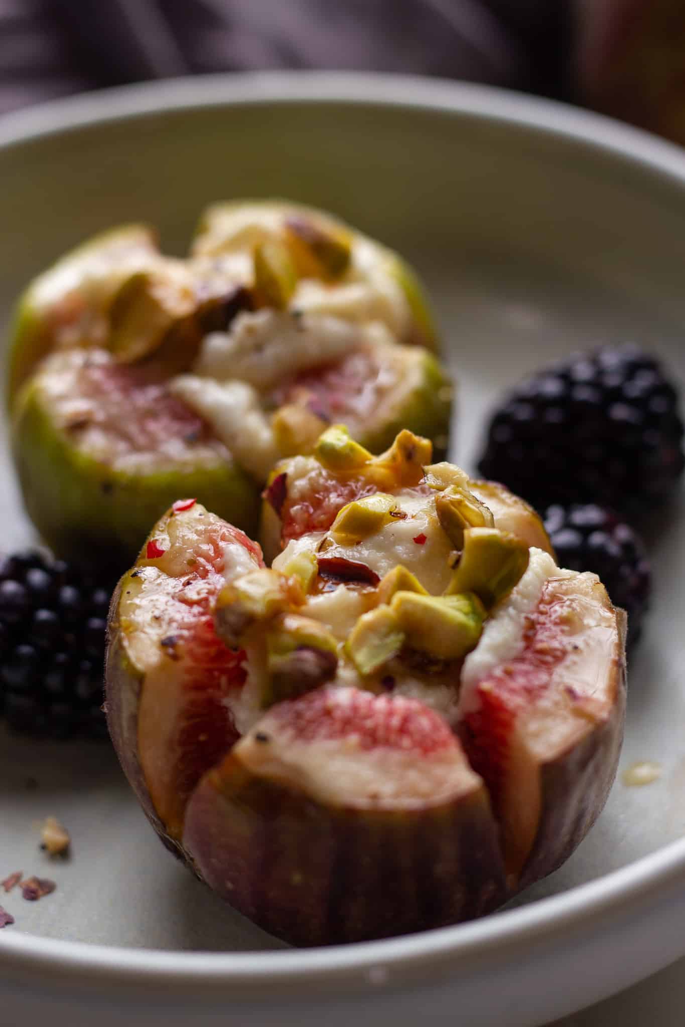 stuffed roasted figs with pistachios and honey served in a small plate with blackberries on the side.