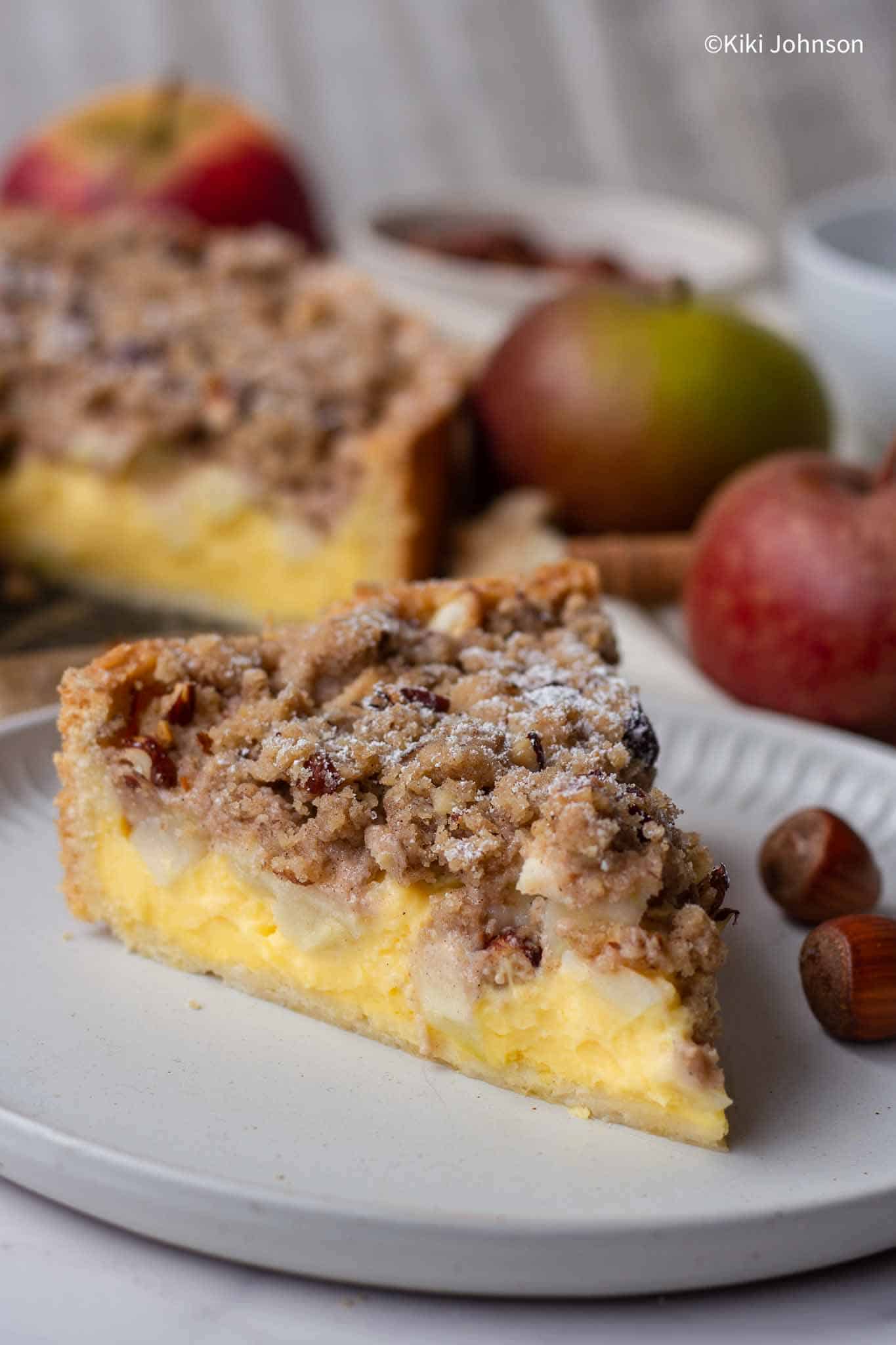 a slice of german apple cake with custard and apple chunks topped with streusel topping. 