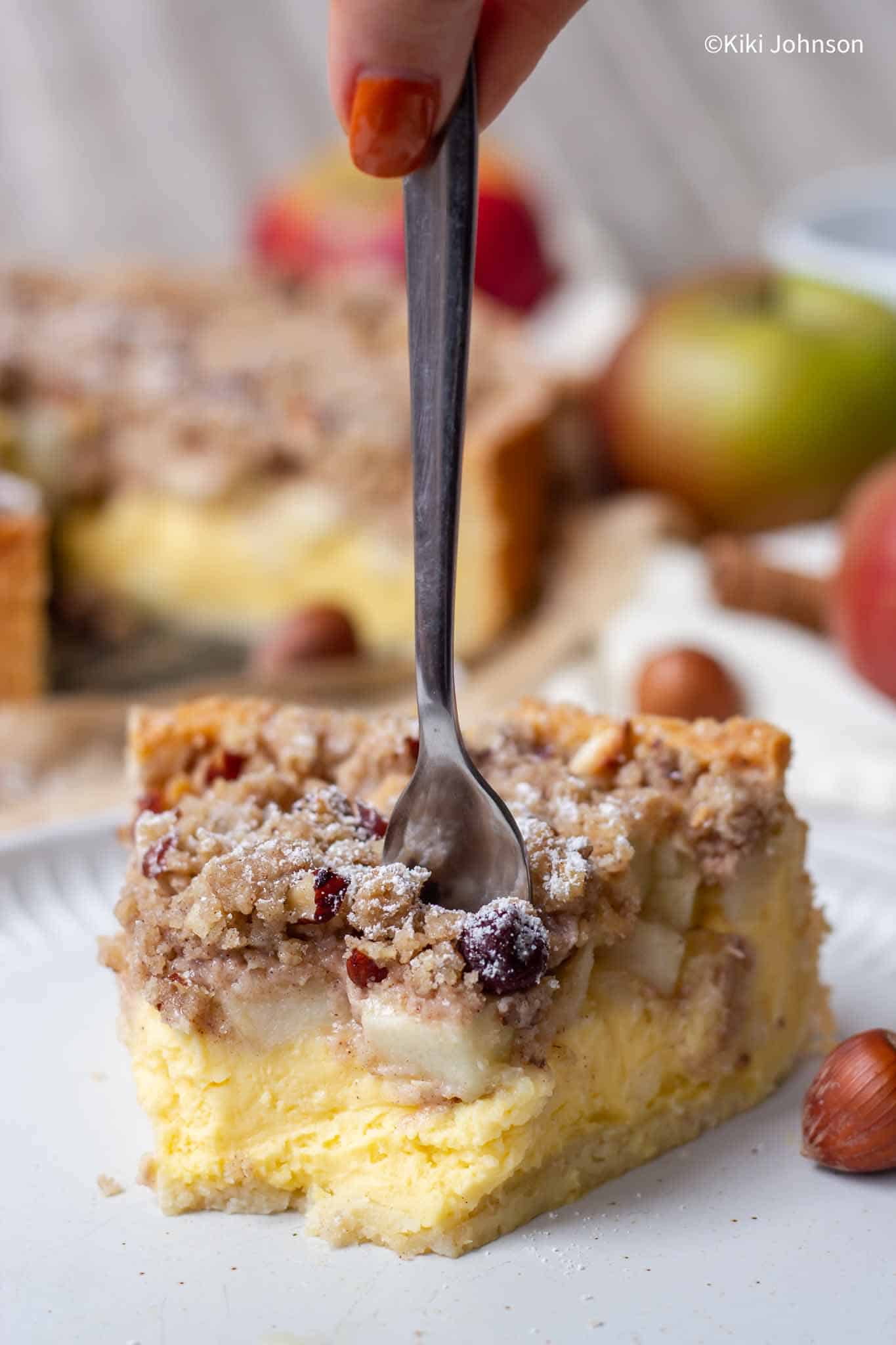 a fork being inserted into a piece of German Apple Cake with Custard and Hazelnut Streusel.