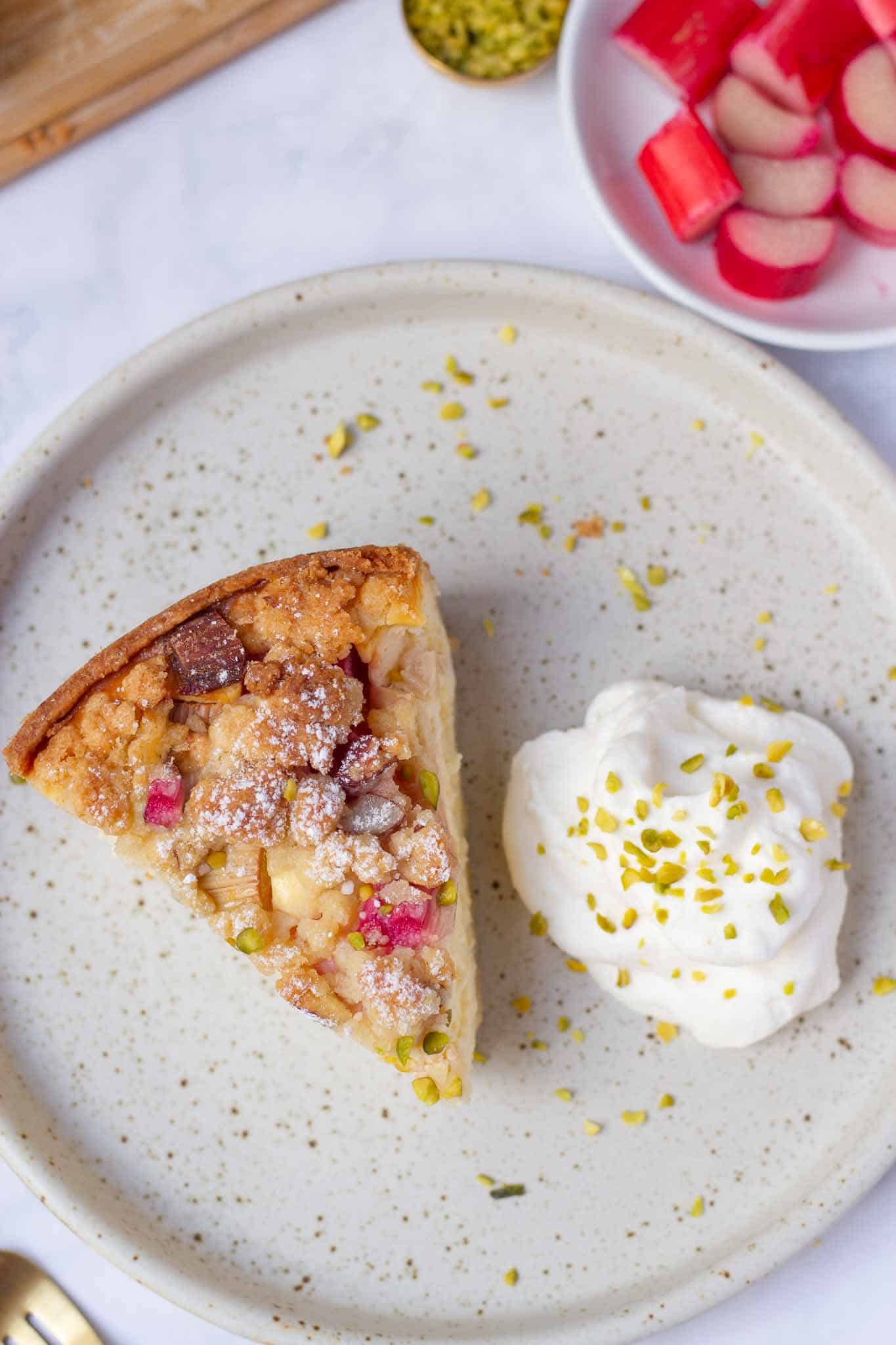 A piece of grandma's cheesecake with rhubarb and streusel on a cake plate next to a dollop of cream. You can also make the cheesecake with raspberries or currants.