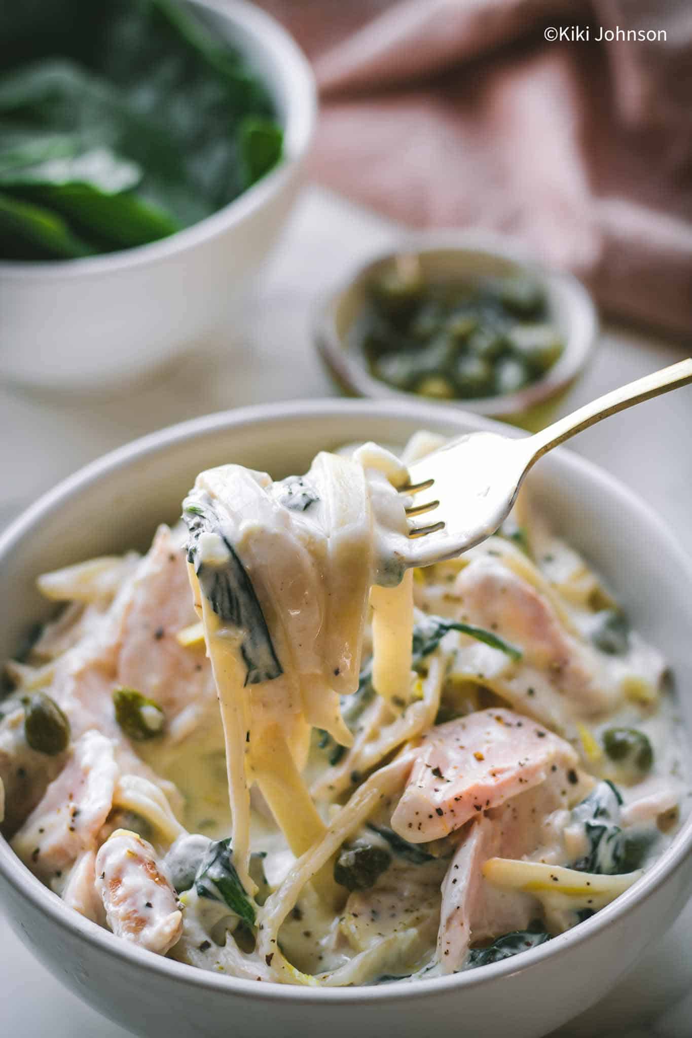 eine Schüssel Lachs Nudeln mit Spinach und Sahnesauce dekoriert mit Kapern und Zitronenschale