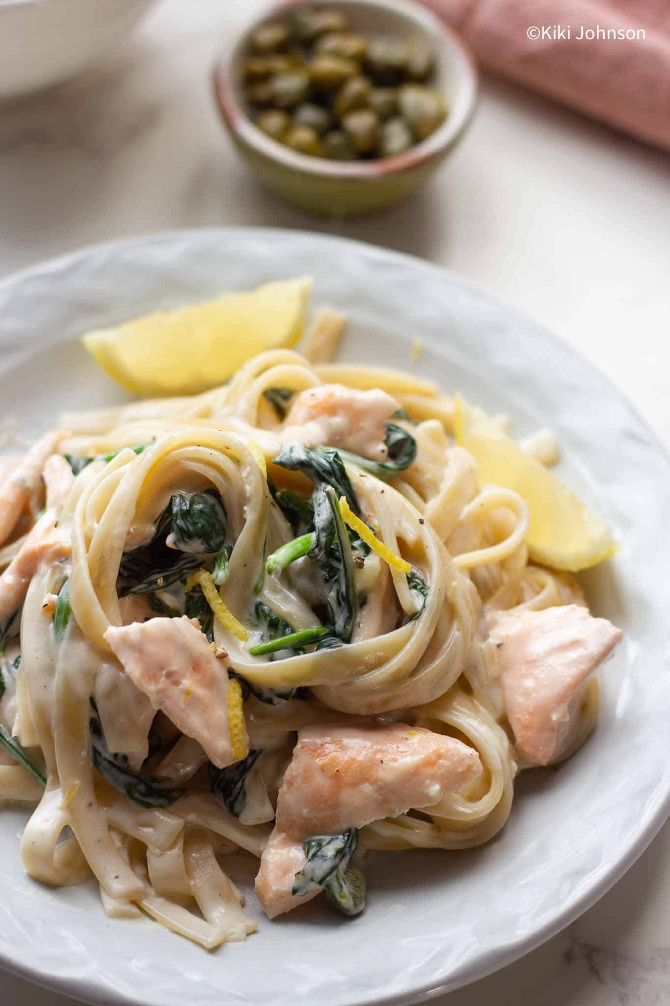 ein Teller mit Bandnudeln mit Lachs, Spinar und Zitronen Weißweinsauce mit Zitronenschnitzen an der Seite