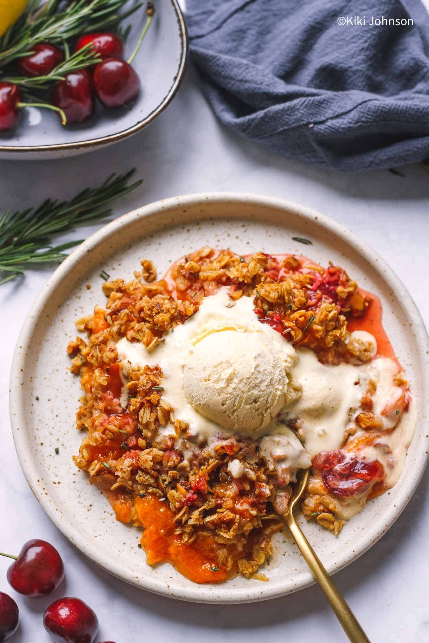 A serving of fresh cherry & apricot crumble with rosemary and crunchy oats topping. Gluten-free and can be made vegan! 