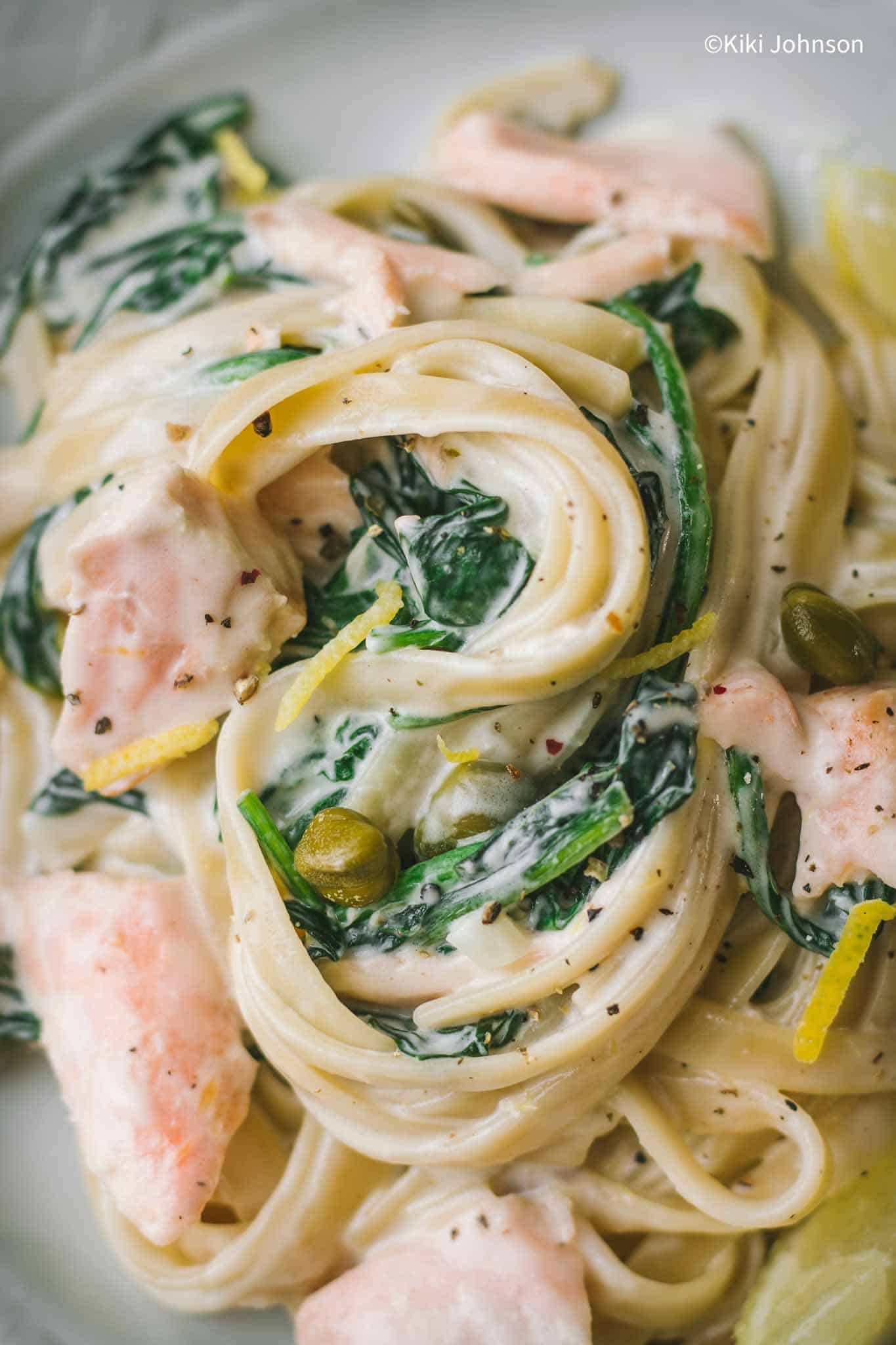 ein Teller Tagliatelle mit Lachs und Spinat in Sahnesauce mit Kapern und Zitronenschale dekoriert.