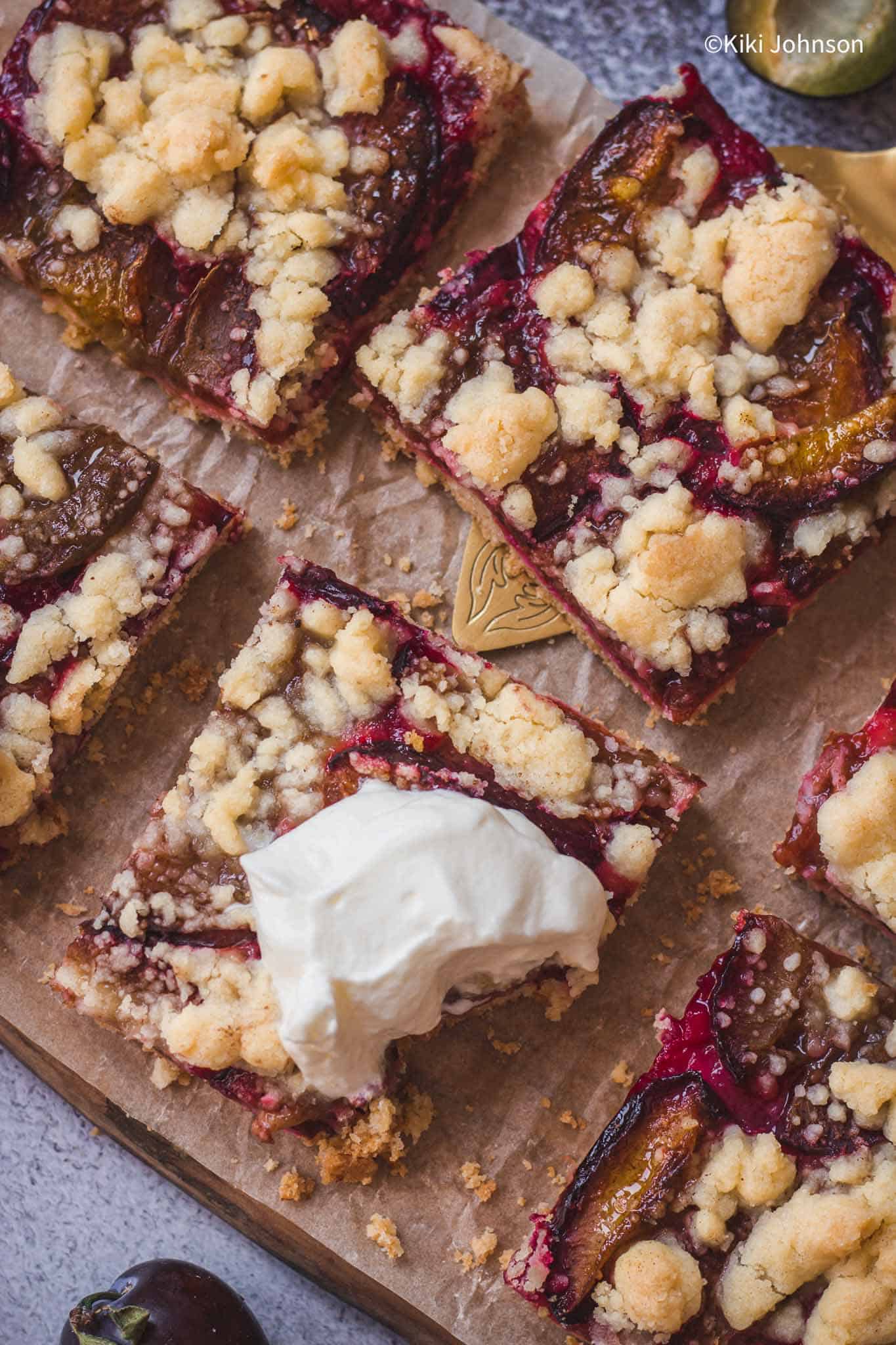 ein Stück bayrischer Zwetschgendatschi mit Streusel auf einem Holzbrett mit einem Klecks Sahne serviert.