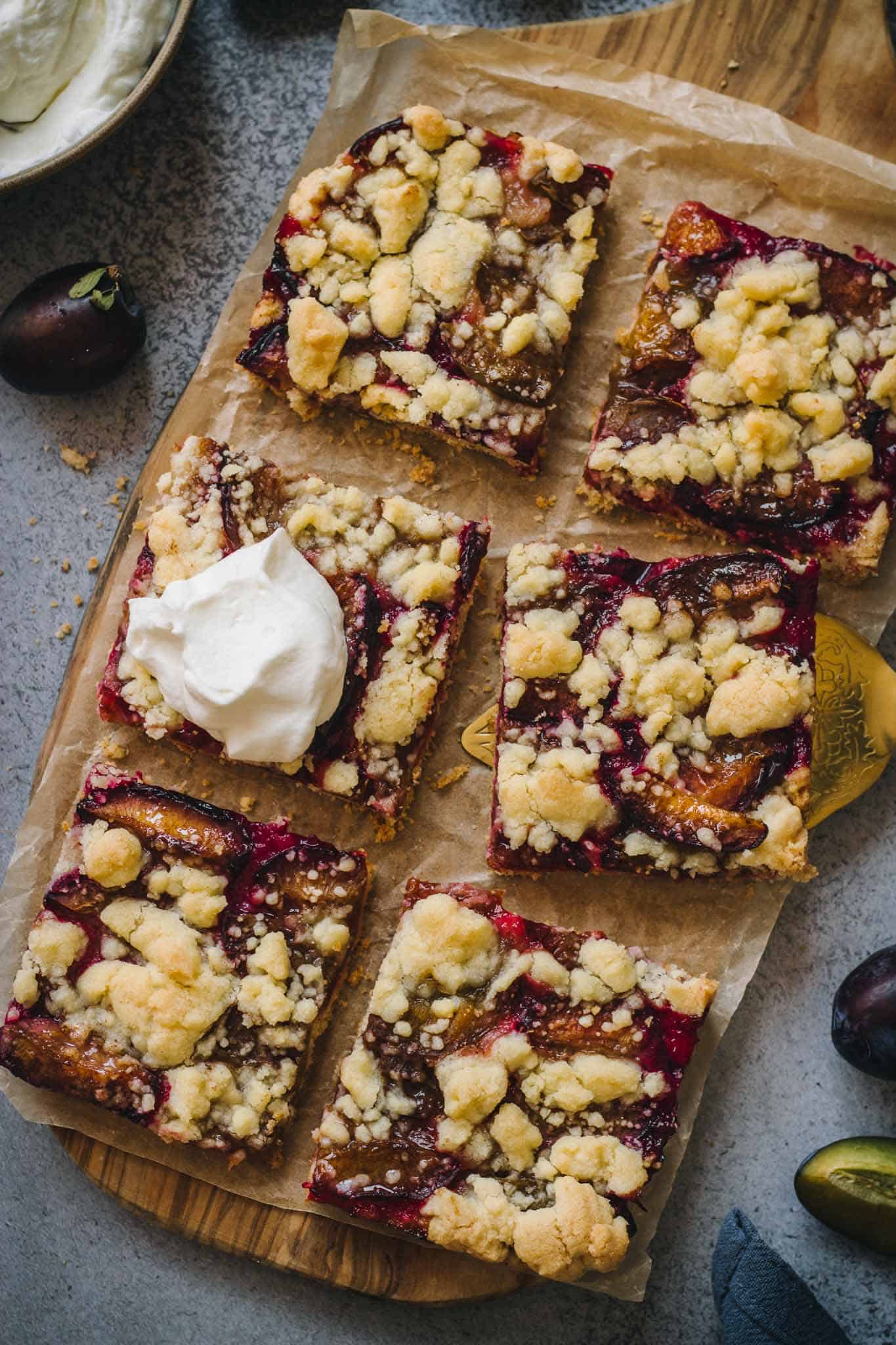 6 pieces of German Zwetschgendatschi Plum Cake with streusel topping on a sheet of baking paper.