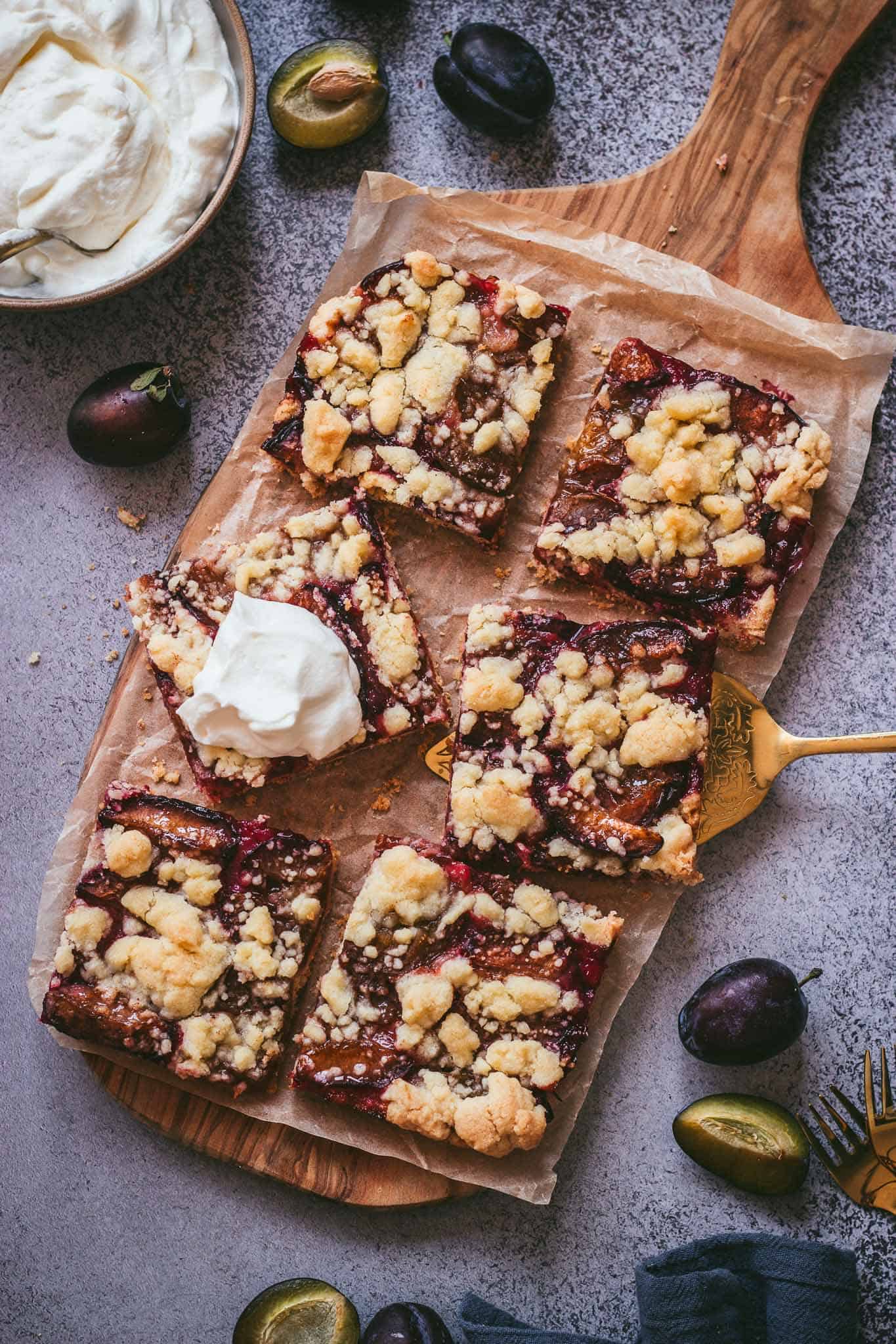 traditional German plum cake topped with crunchy streusel  and whipping cream on a wooden board.