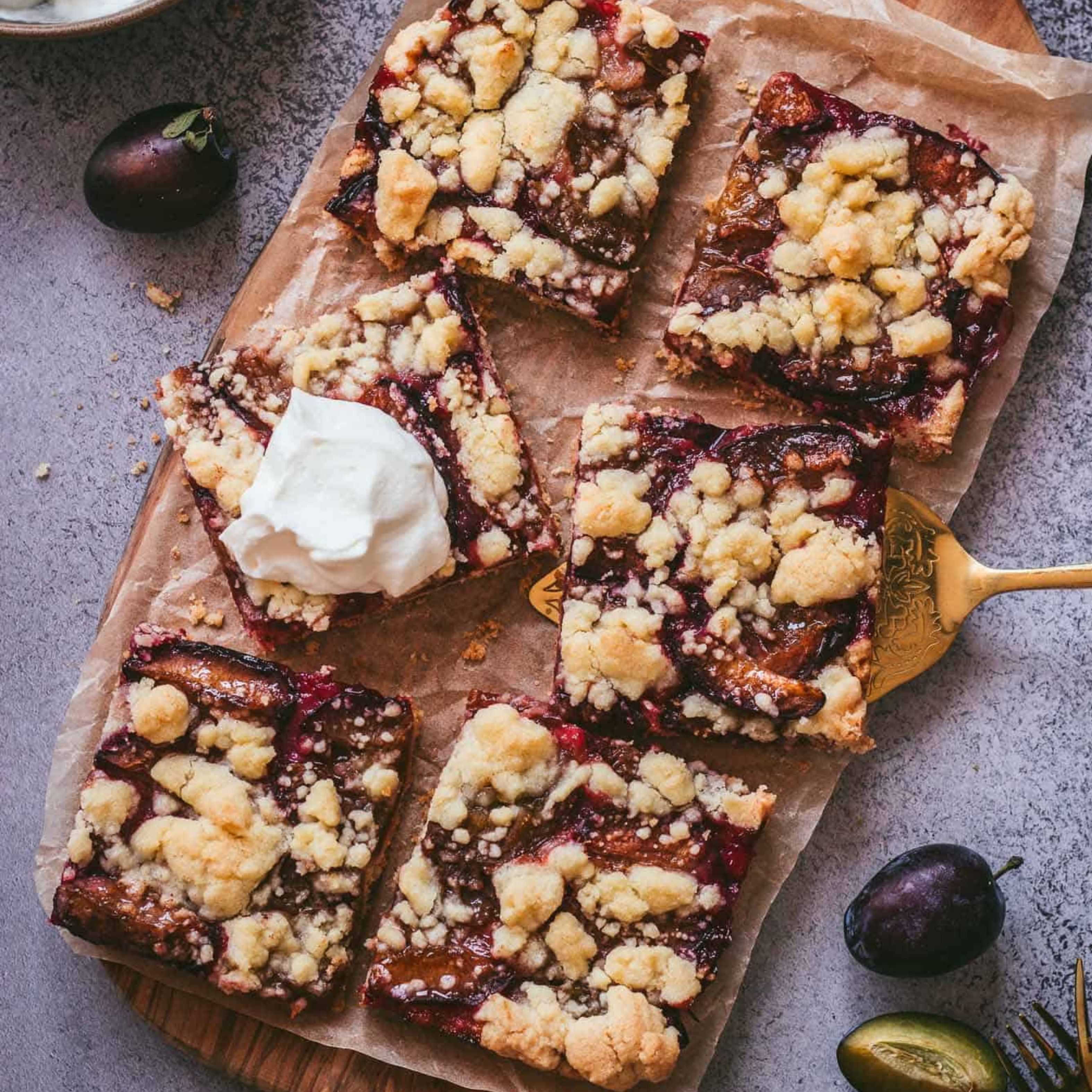 Zwetschgendatschi mit Streusel auf einem Holzbrett mit einem Klecks Sahne serviert.