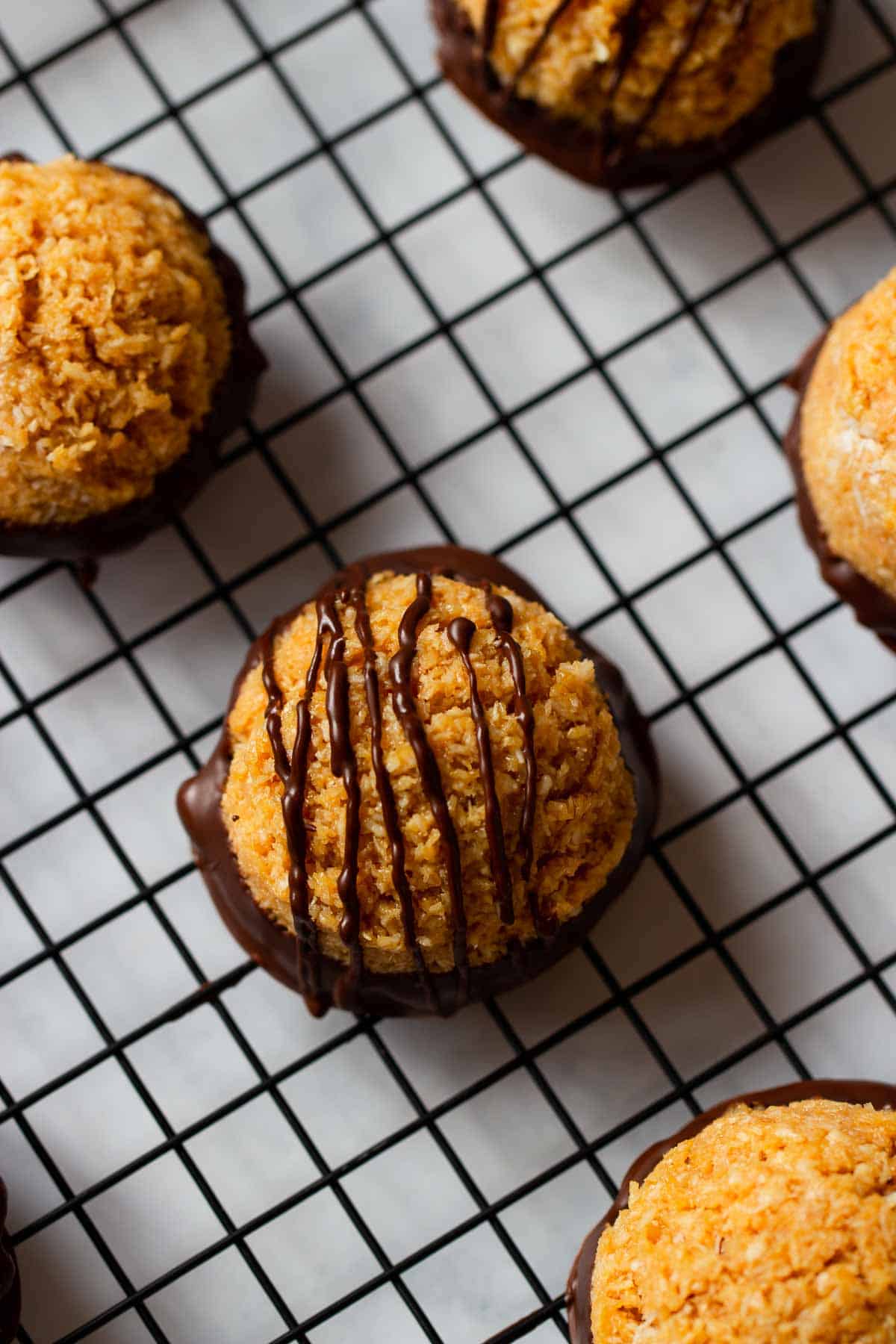 close up of dulce de leche coconut macaroons drizzled with dark chocolate on a cooling rack. 