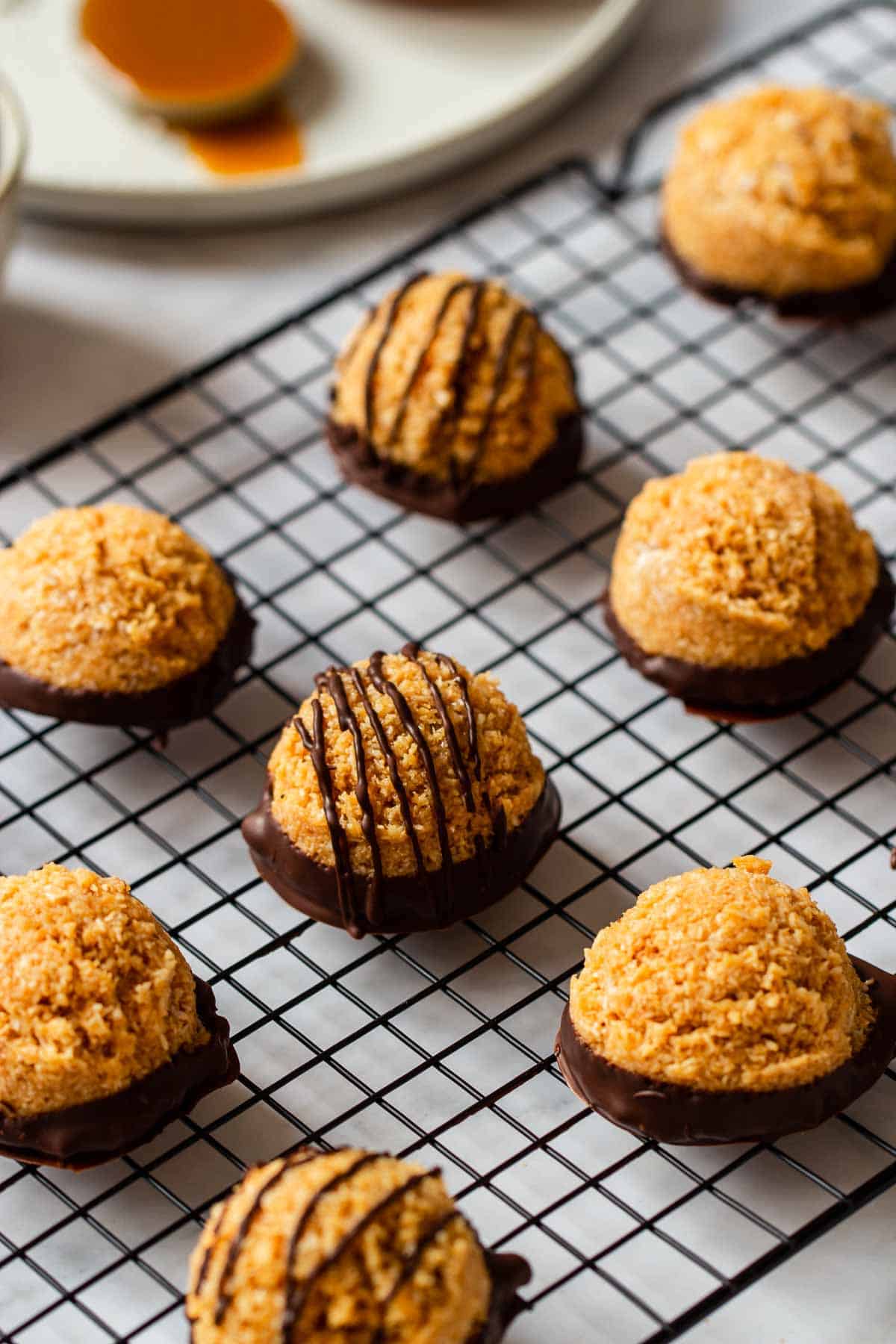 dulce de leche coconut macaroons drizzled with dark chocolate on a cooling rack. 