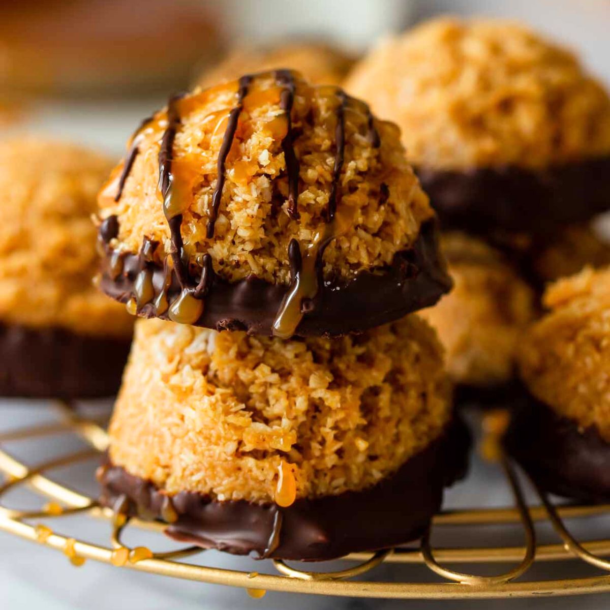 zwei Dulce de Leche Kokosmakronen ohne Backen mit dunkler Schokolade auf einem goldenen Abtropfgitter