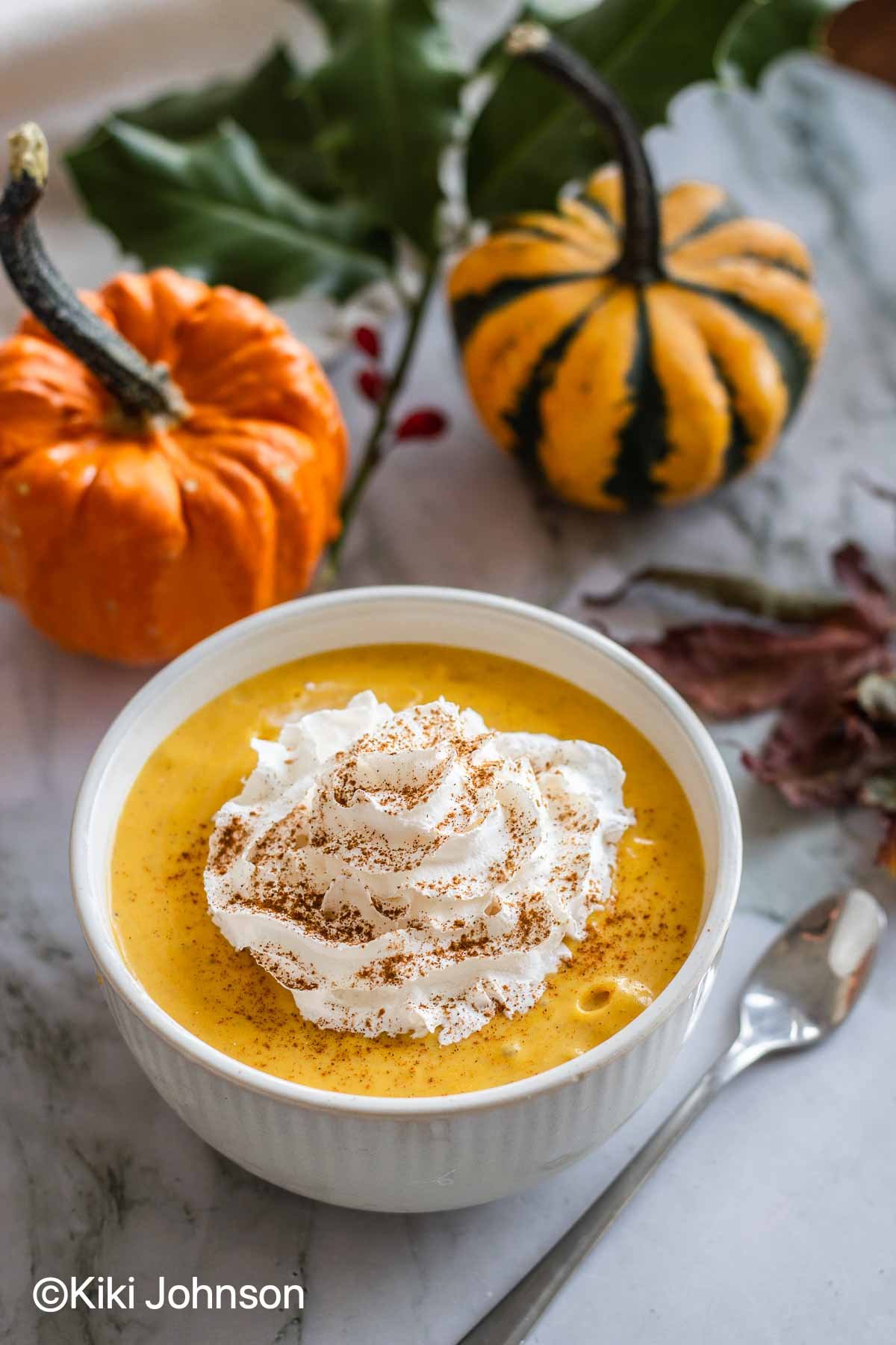 a small white bowl with pumpkin pudding topped with coconut whipped cream and cinnamon.