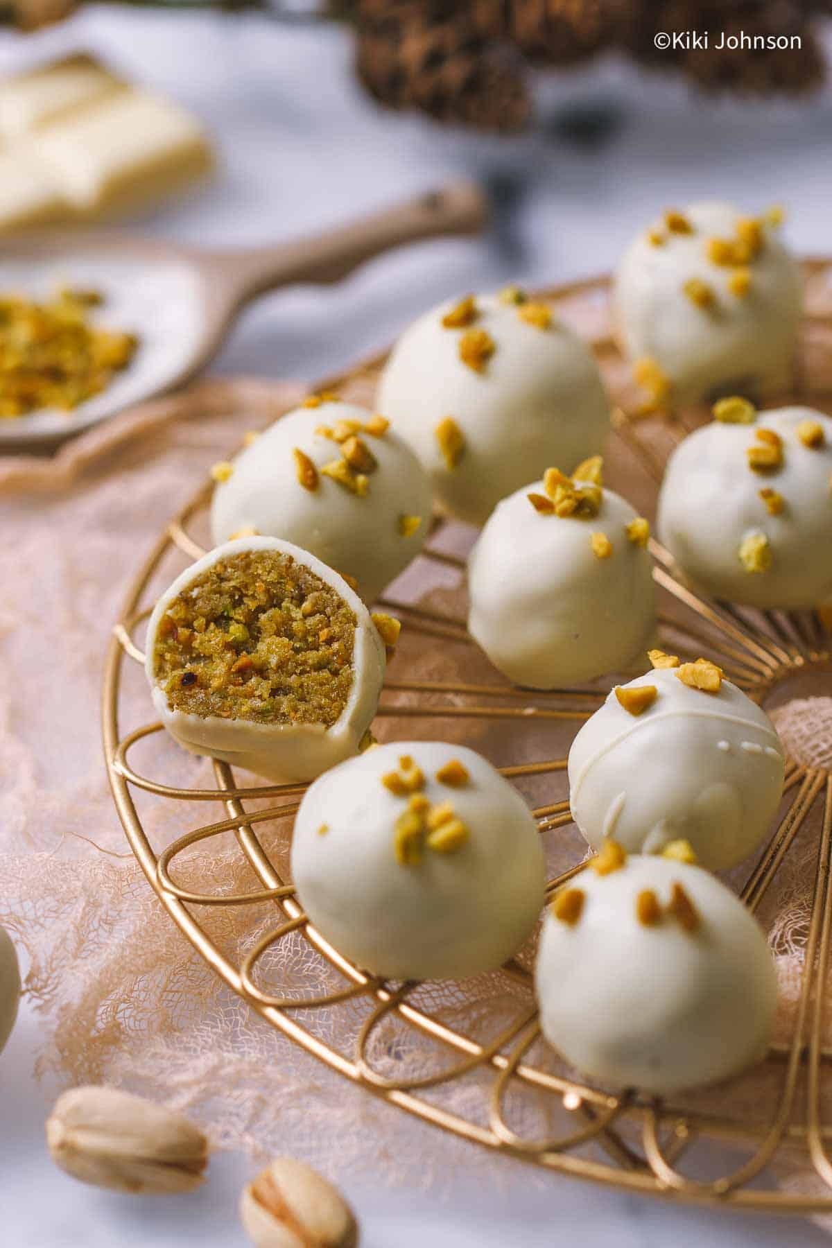 Pistazien Pralinen mit weißer Schokolade auf einem goldenen Gitter mit einer Praline angeschnitten.