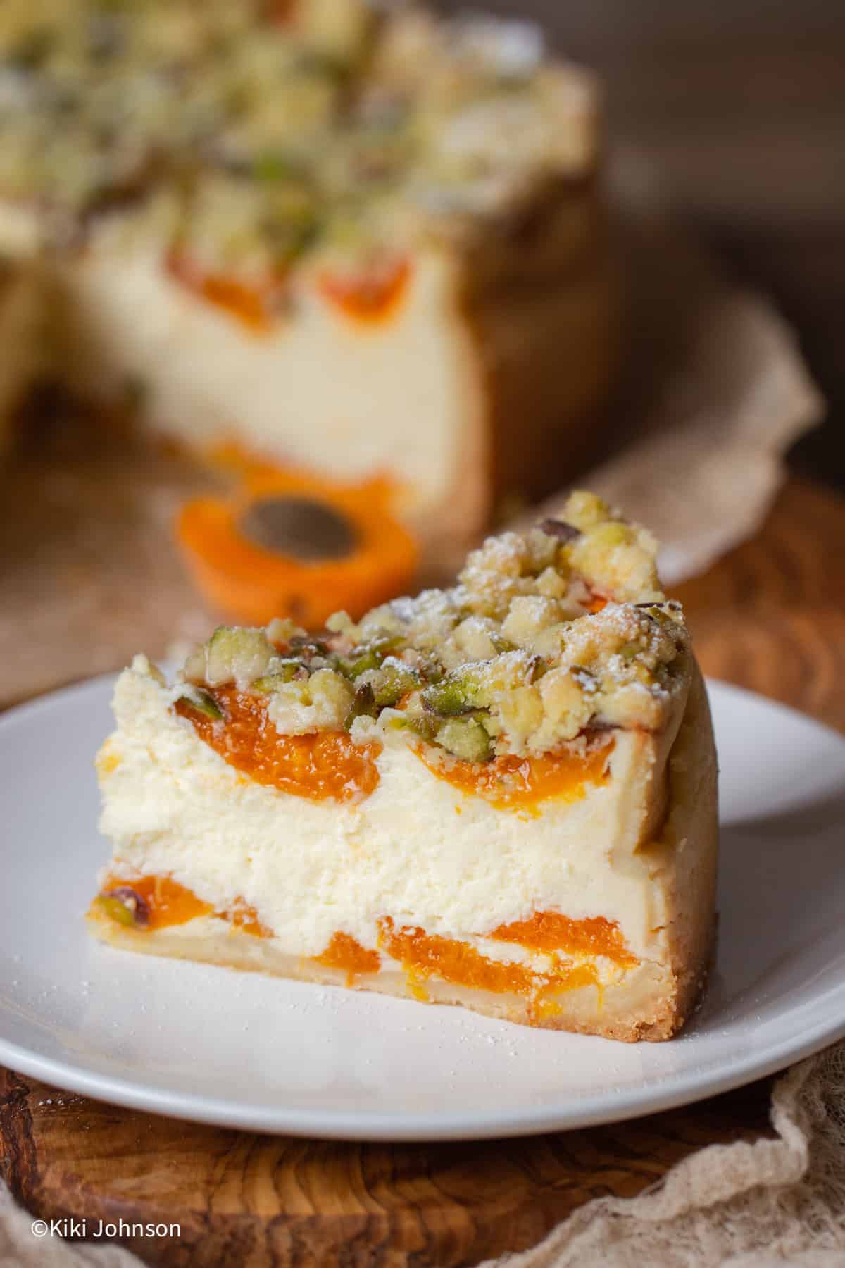 ein Stück Aprikosen Käsekuchen mit Pistazien Streusel auf einem weissen Kuchenteller