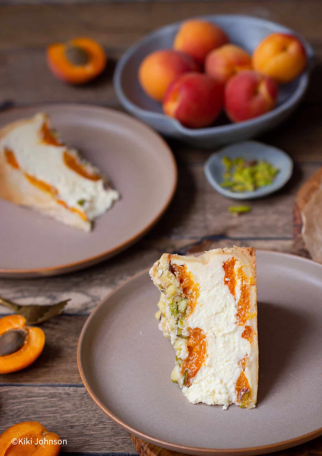 zwei Stücke Marillenkuchen mit Topfen und Pistazien Streusel auf zwei braunen Tellern.