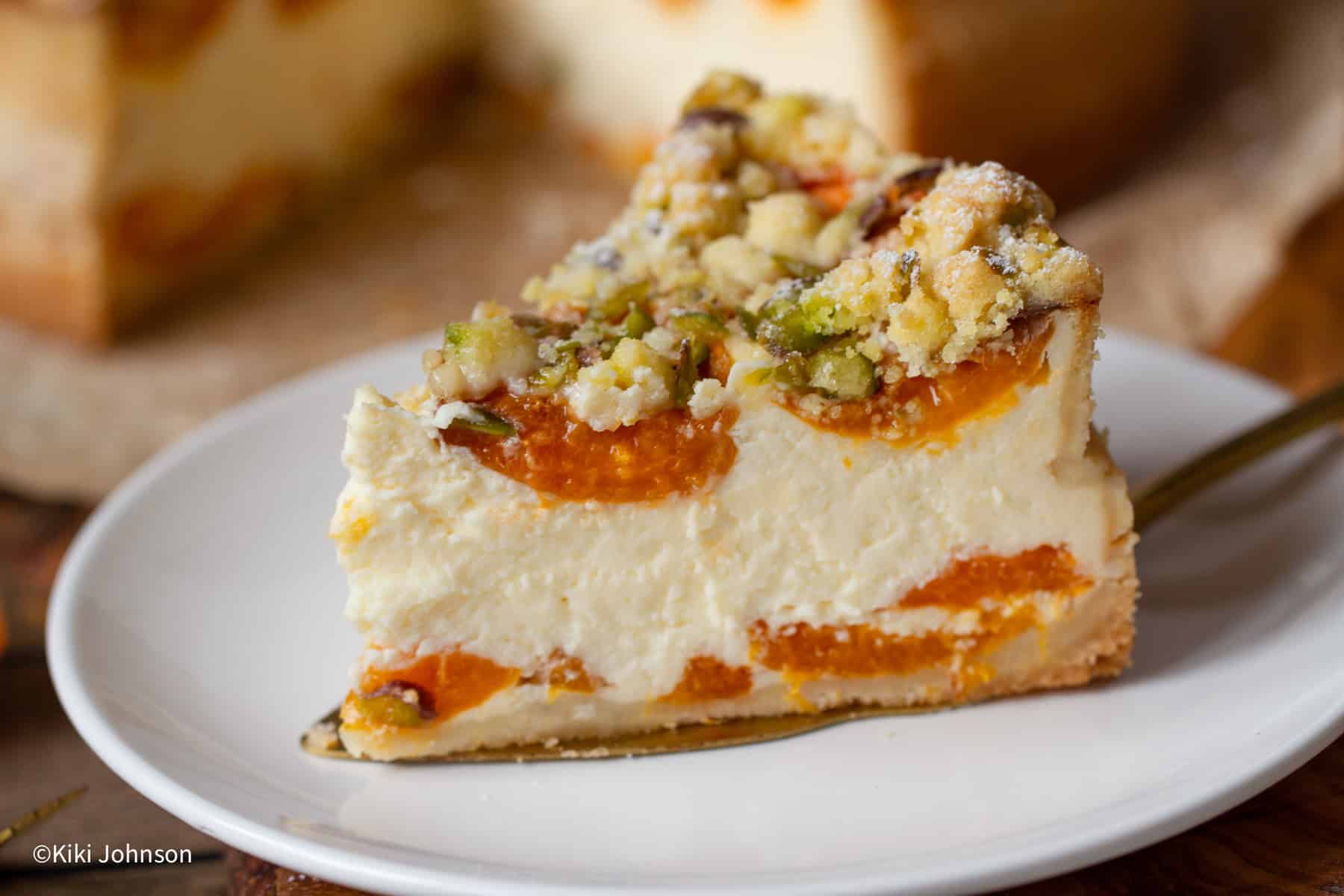 ein Stück Aprikosen Käsekuchen mit Pistazien Streusel auf einem Porzellan Kuchenteller