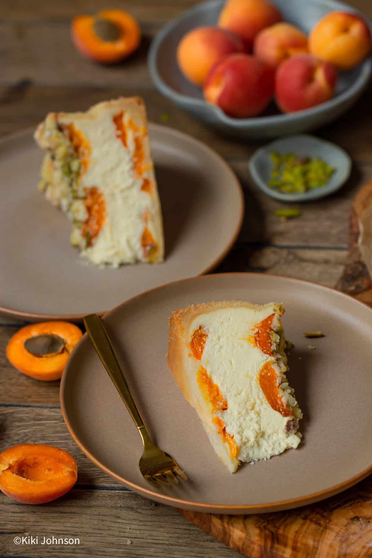 zwei Stück Aprikosen Käsekuchen mit Pistazien Streusel auf zwei braunen Kuchentellern.