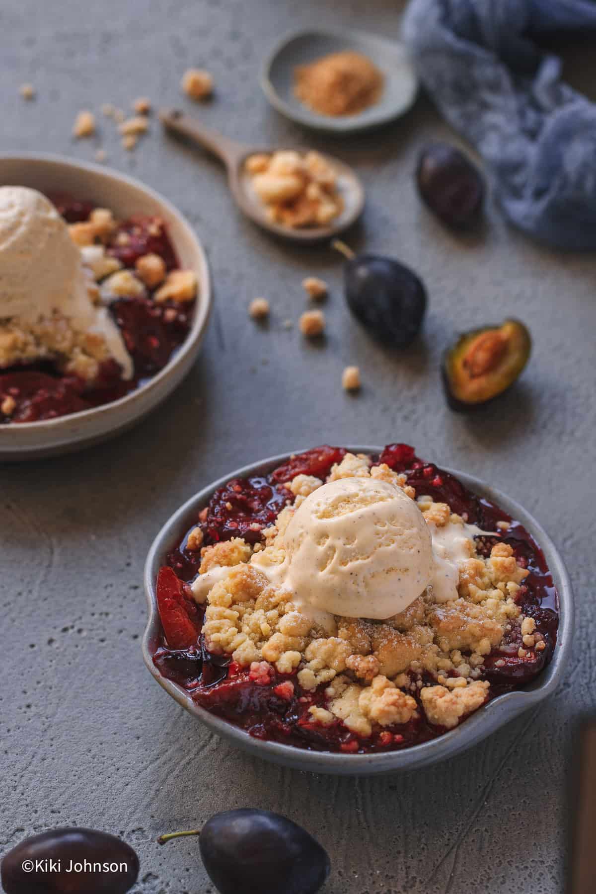 eine Schale mit Zwetschgen Crumble mit Butter Streuseln und einer Kugel Vanilleeies