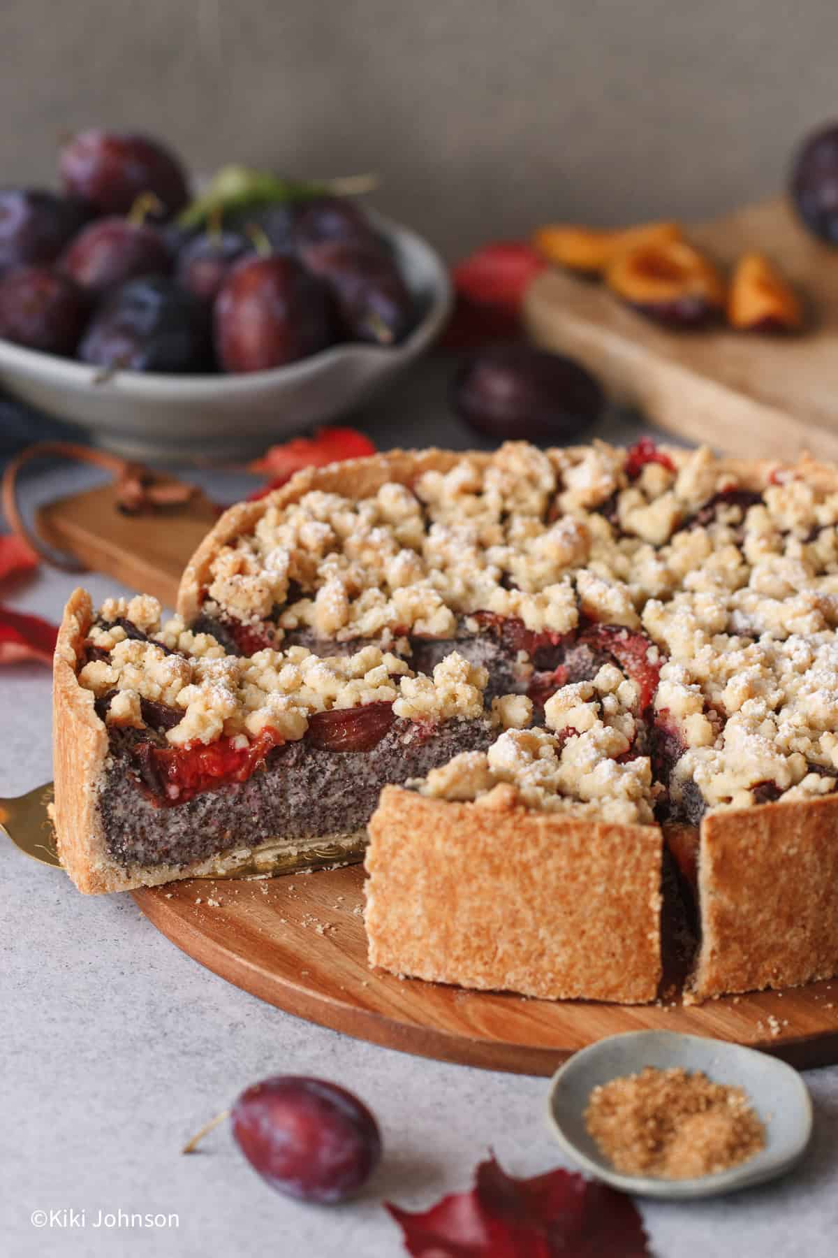 a sliced German poppy seed cake with homemade poppyseed filling and prune plums topped with streusel topping on a wooden board