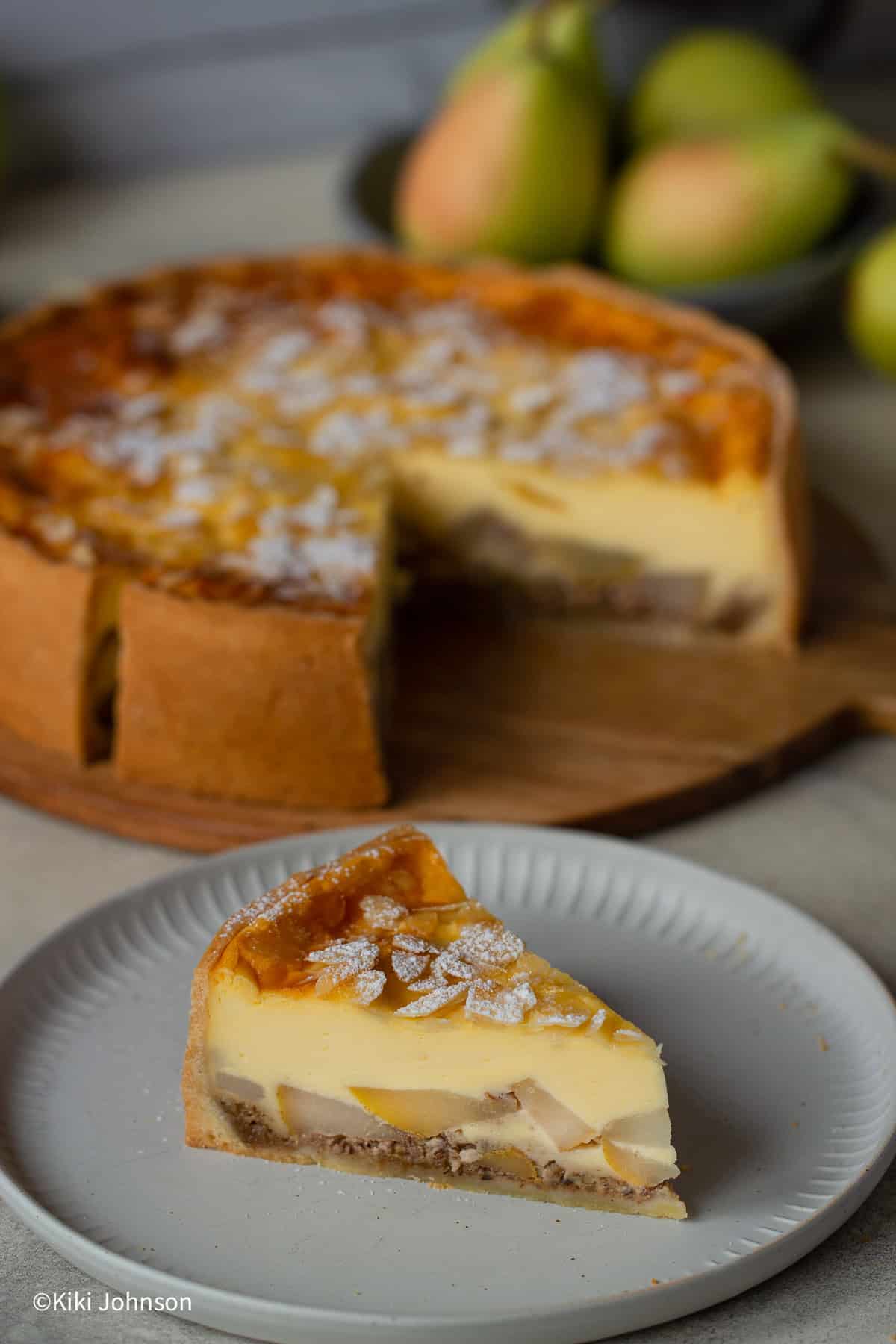 a slice of German pear cake with vanilla custard topped with sliced almonds on a white plate.